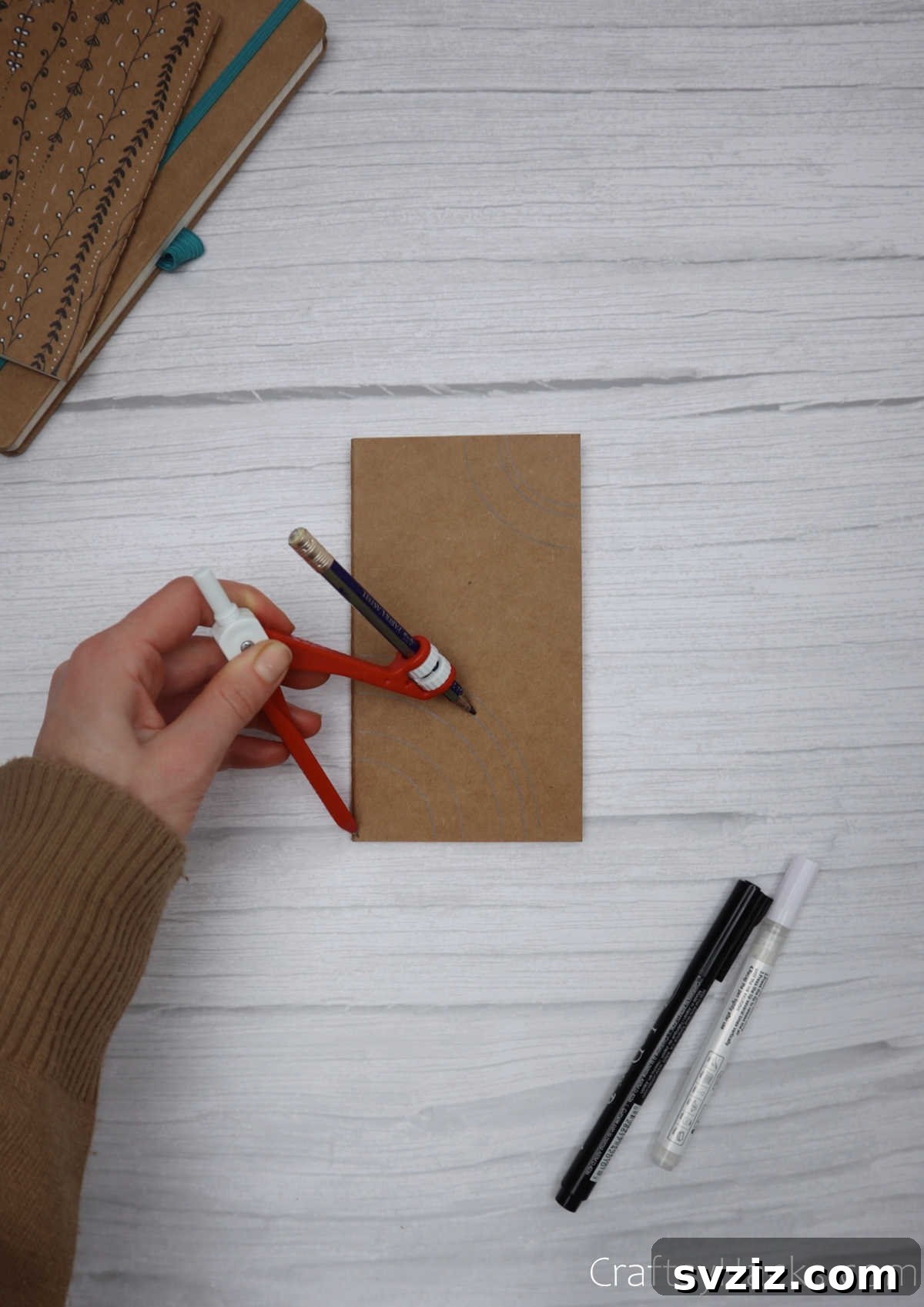 Make Your Journal Cover Unique 20 A hand using a compass to lightly trace concentric circles onto the journal cover, preparing for a mandala design.