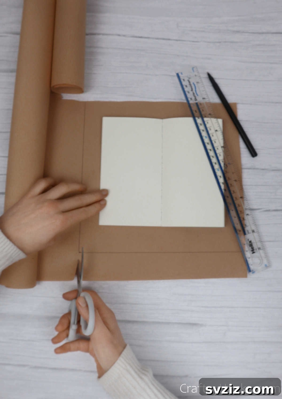 Make Your Journal Cover Unique 5 A notebook opened flat on a sheet of kraft paper, with scissors poised to cut the paper to size, leaving ample margins.