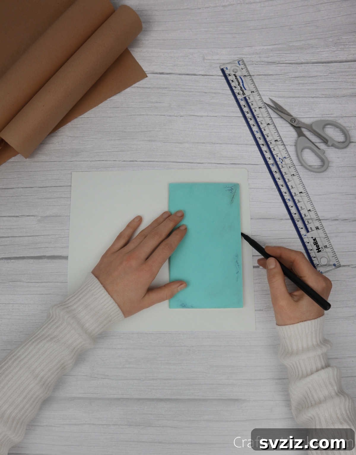 Make Your Journal Cover Unique 7 A closed notebook being traced onto a plain sheet of paper with a pen, preparing for the inner cover panels.