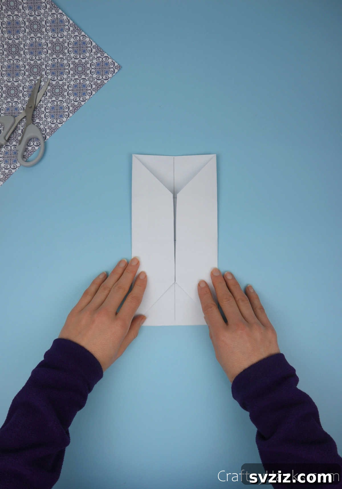 The paper with both its left and right sides folded inwards towards the center, neatly enclosing the pre-folded corner triangles, forming a compact rectangular shape.