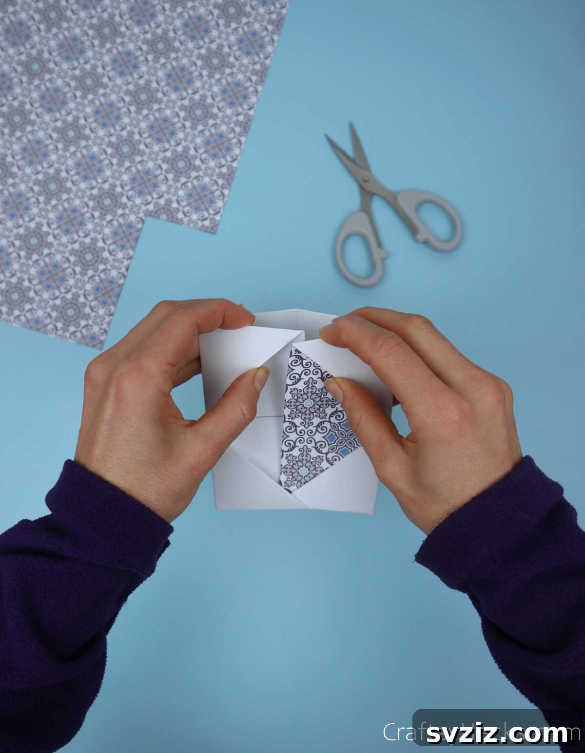 A piece of patterned decorative paper being carefully and snugly tucked into the diamond-shaped opening of a paper module, adding a colorful accent.