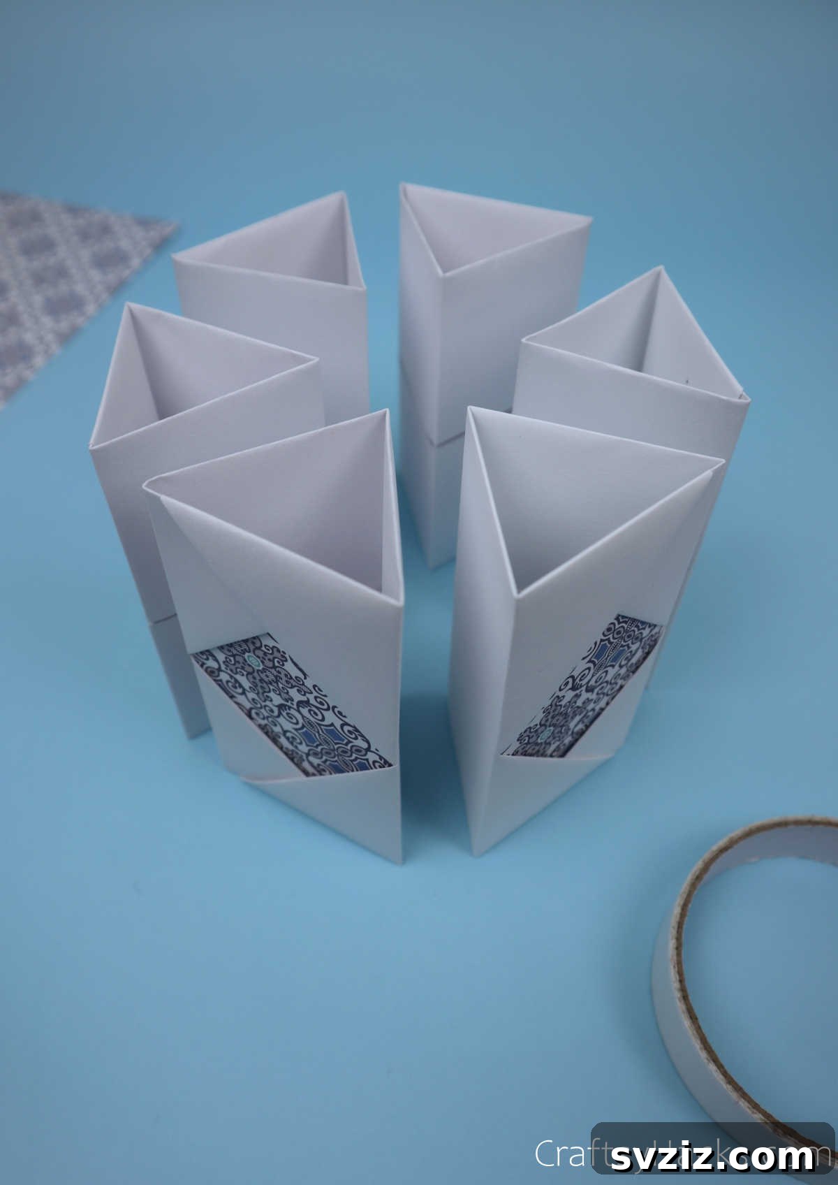 Six completed paper modules standing upright in a semi-circular arrangement, forming the initial shape of the hexagonal pencil holder before final joining.