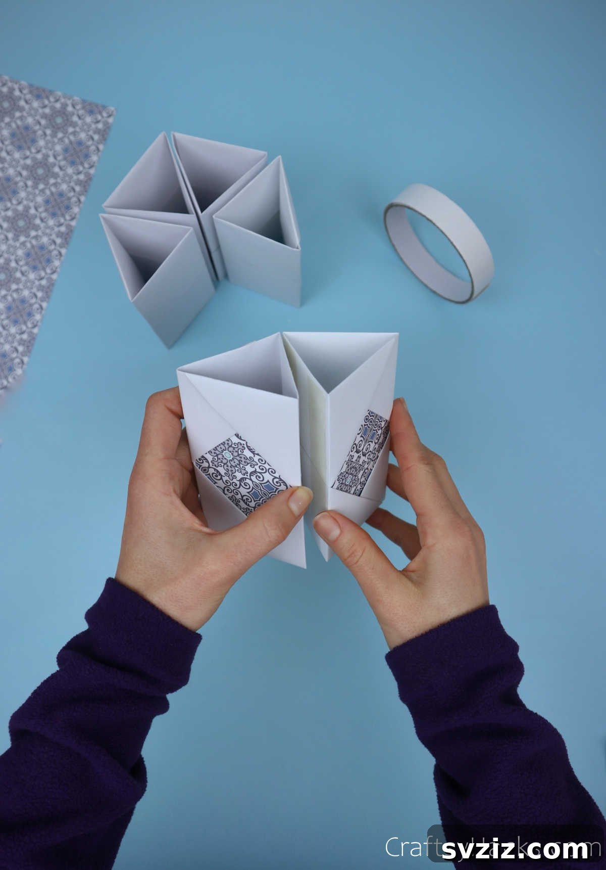 Two paper modules being carefully joined together using double-sided tape, illustrating the precise assembly technique for the pencil holder.
