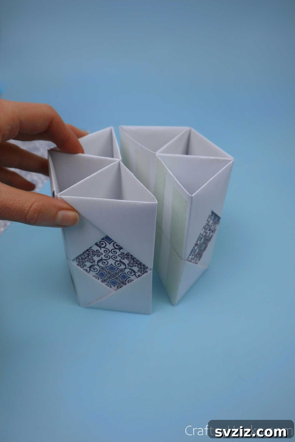 Several paper modules already joined, with the final module being attached to complete the entire hexagonal structure of the pencil holder.