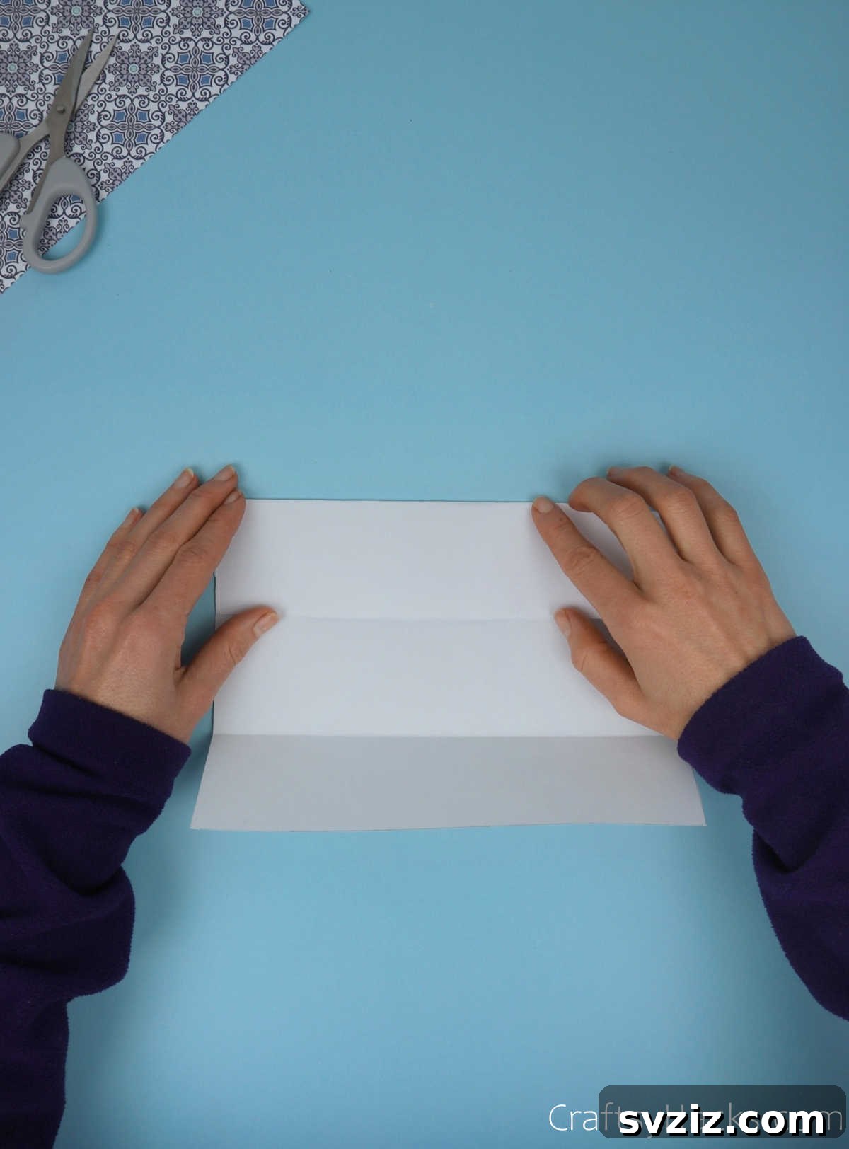 The top half of the paper being folded downwards to align with the central crease, after the bottom half has been folded, creating a symmetrical pattern.