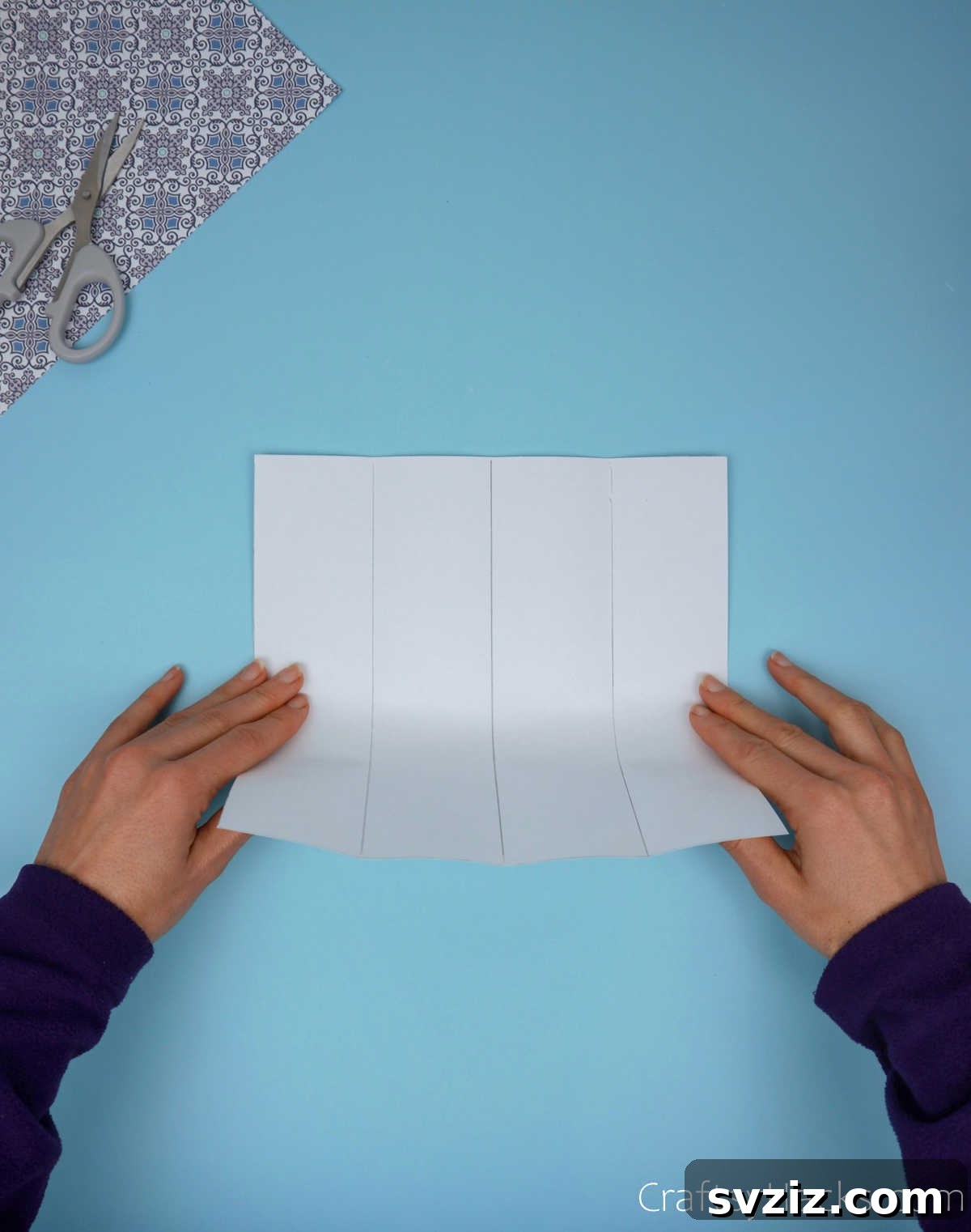 A square paper sheet being folded vertically in half, emphasizing precision in alignment to form a clear central vertical crease.