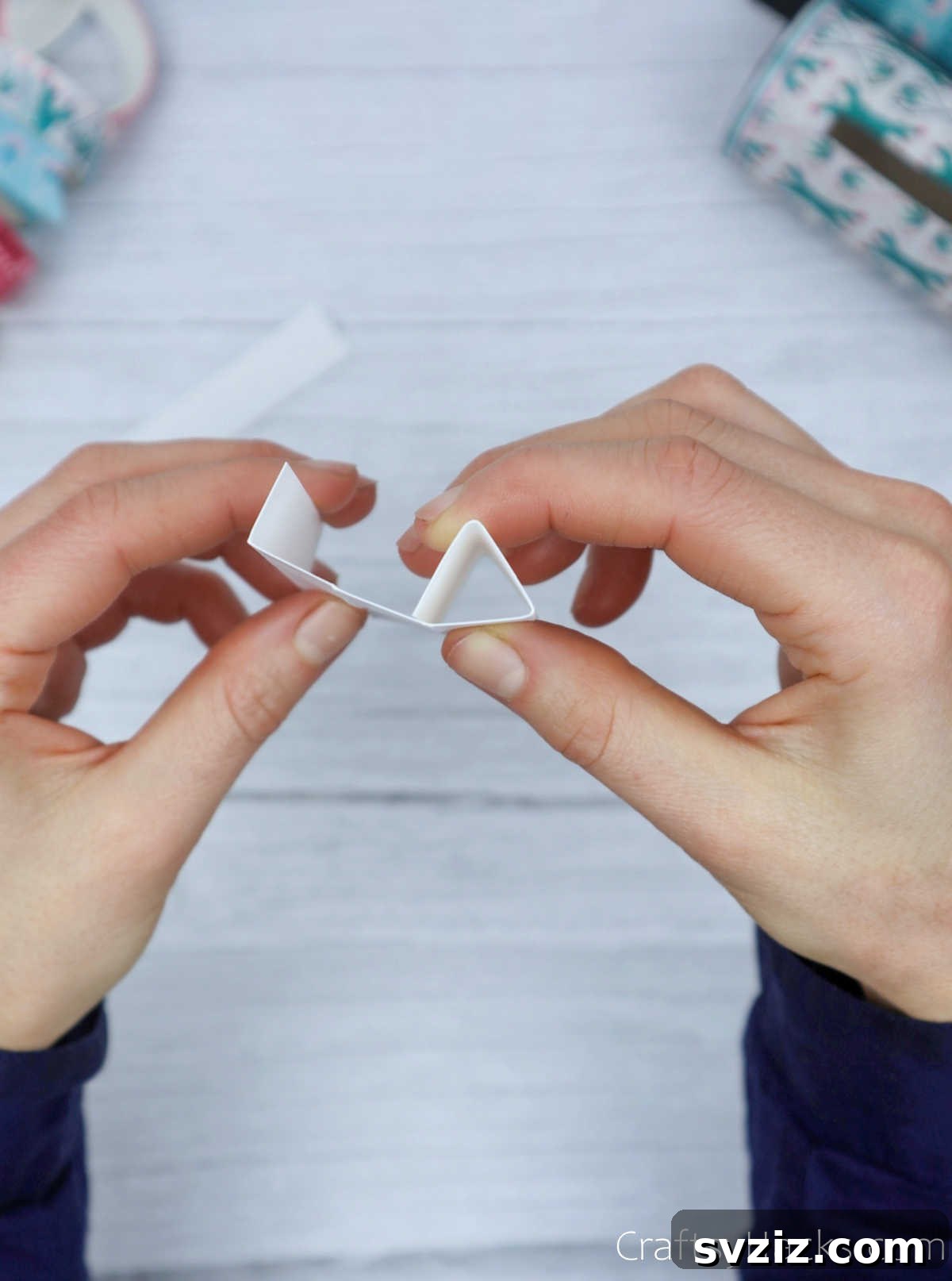 Roll Your Own Phone Stand from a Toilet Paper Tube 22 A hand demonstrating the final fold to create a perfect paper triangle, ready to be secured.