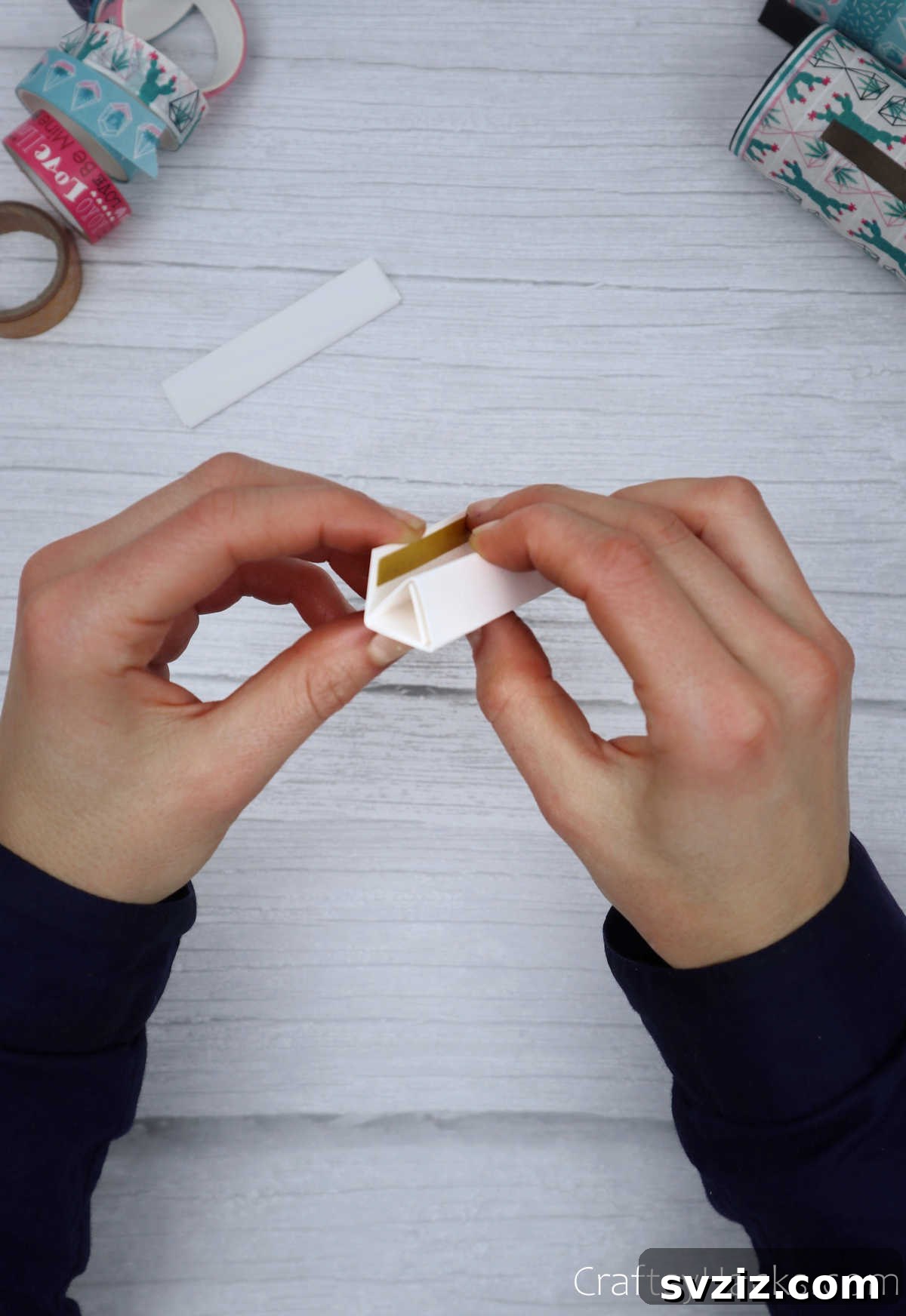 Roll Your Own Phone Stand from a Toilet Paper Tube 23 A hand holding a completed paper triangle, with the open end secured, ready for attachment.
