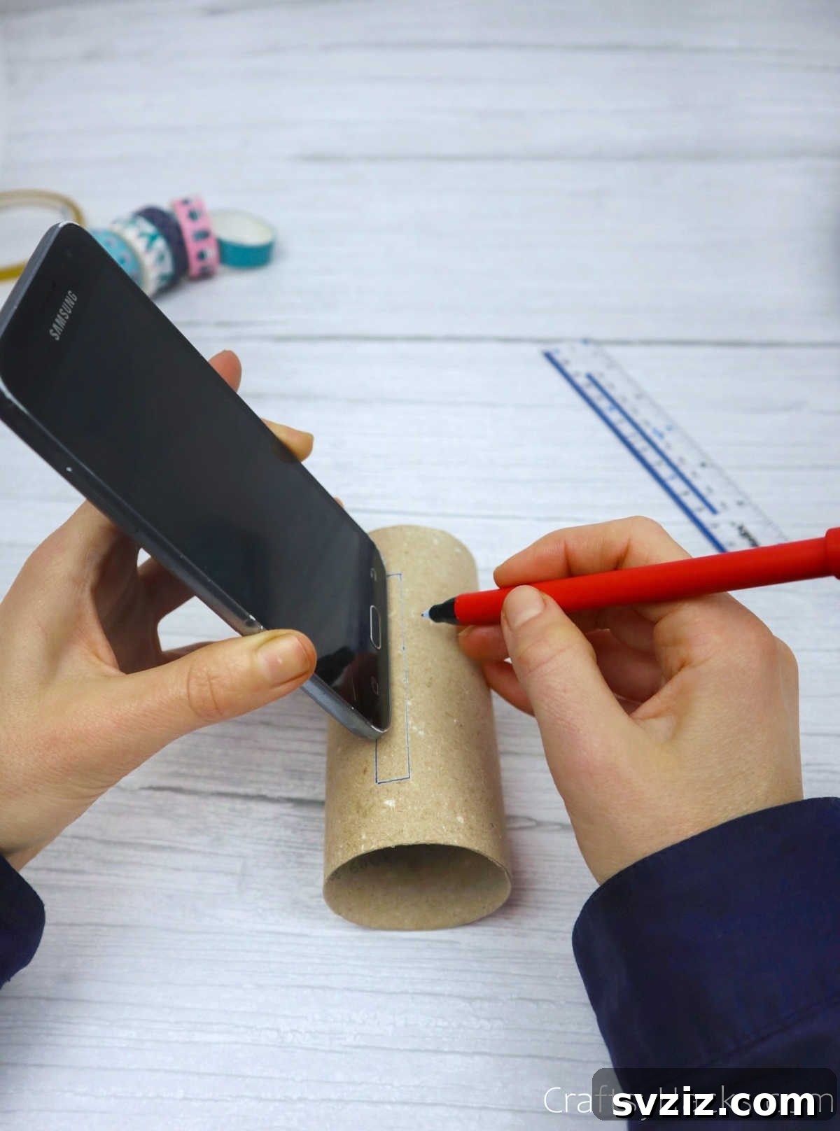 Roll Your Own Phone Stand from a Toilet Paper Tube 6 A hand tracing the outline of a phone onto a toilet paper roll with a marker.