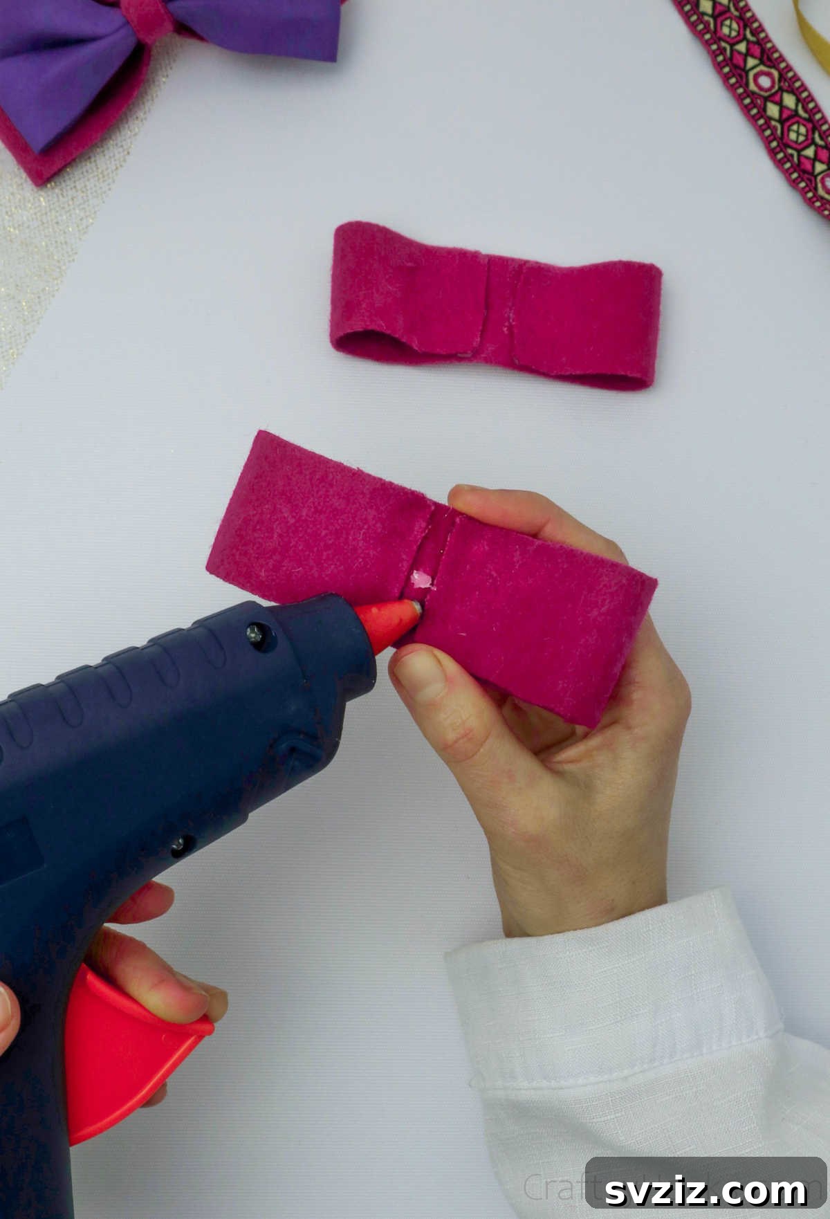 A small dot of hot glue applied to the center of a felt bow, preparing it for the pinching technique