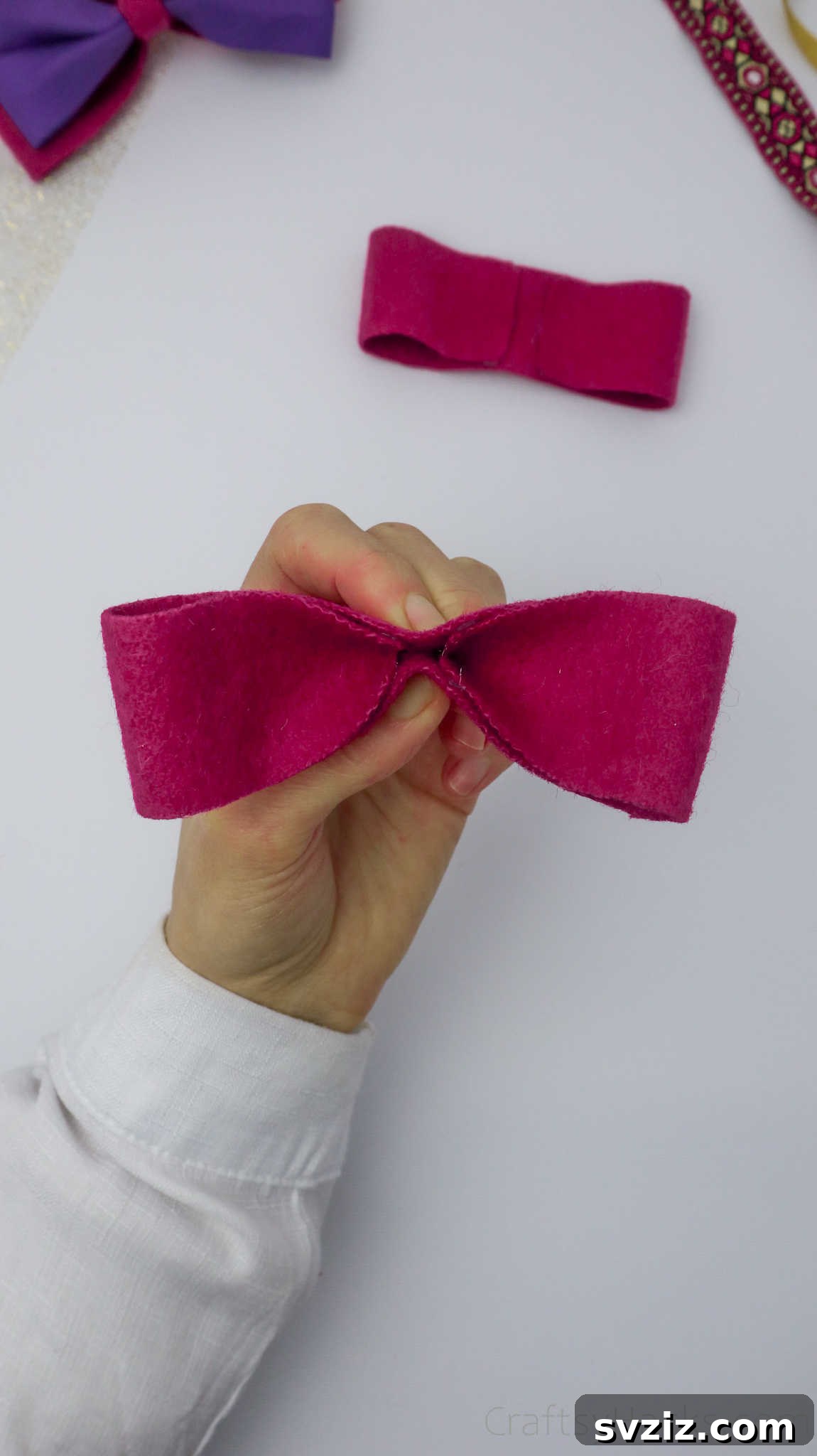 Hands demonstrating the pinching technique on a pink bow, shaping it for added definition and elegance
