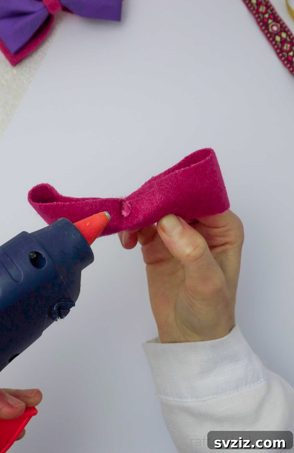 Hot glue being applied to one pink felt bow, indicating where to attach the second layer for a cohesive design