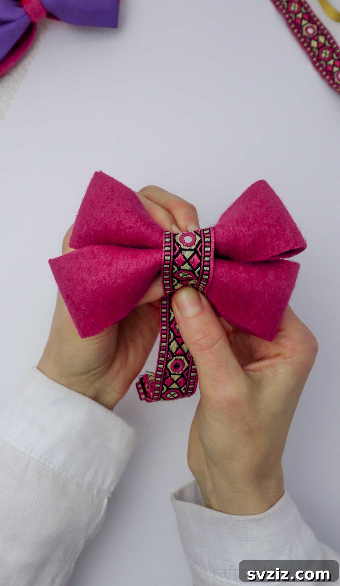 A decorative ribbon being wrapped around the center of a layered pink bow, creating a polished finish