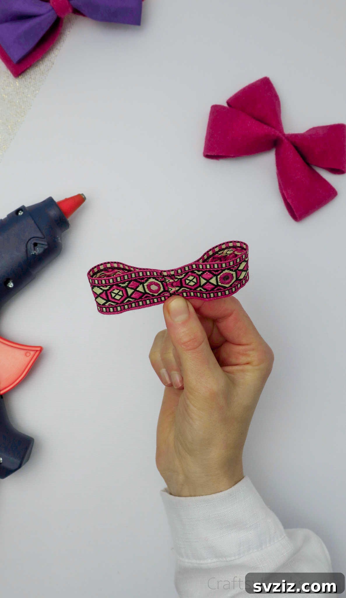 Hot glue being applied to the decorative ribbon before it's wrapped around the bow, ensuring a secure attachment