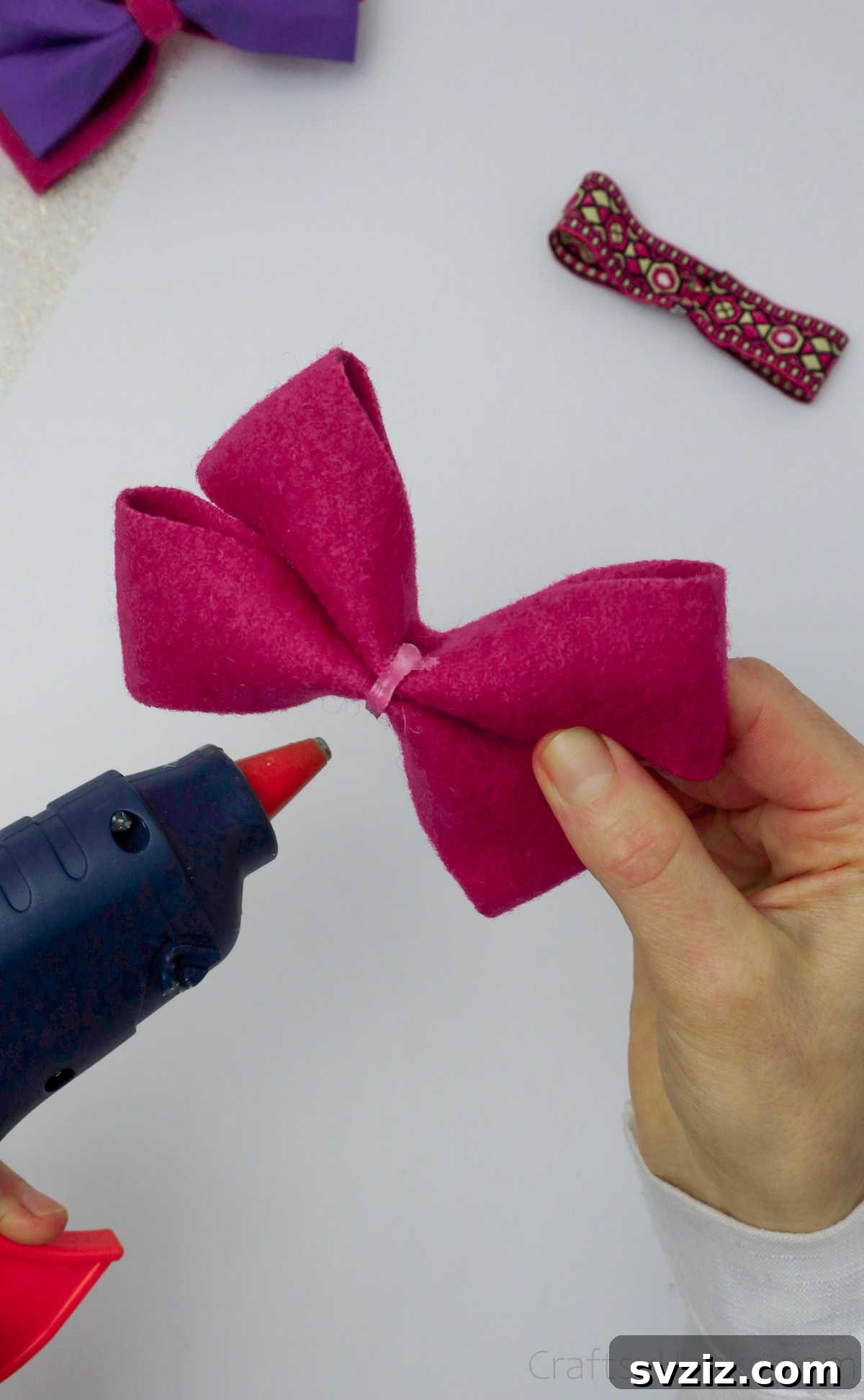 Applying hot glue to the back of the layered pink bow, preparing for the decorative center ribbon