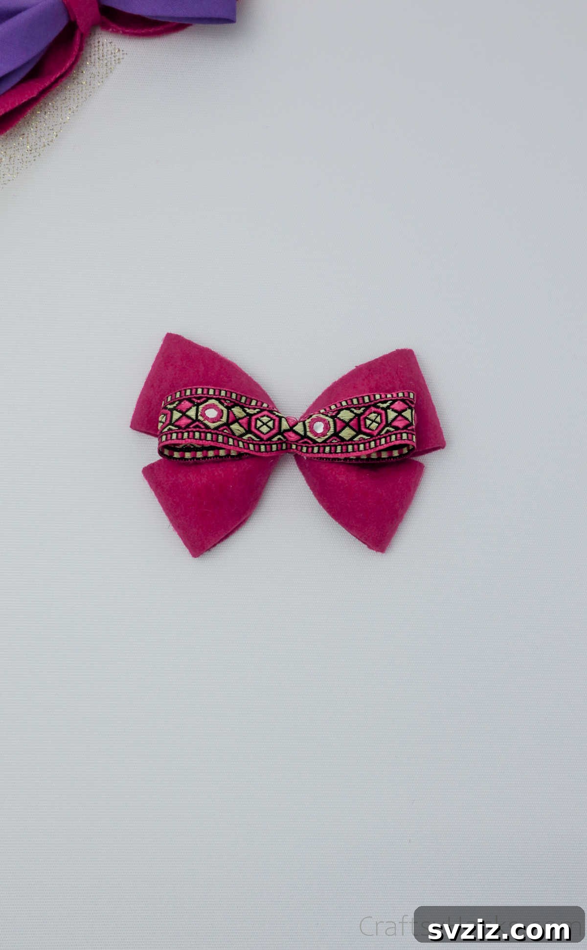 The decorative ribbon being securely glued to the center of the pink bow, finalizing its beautiful design