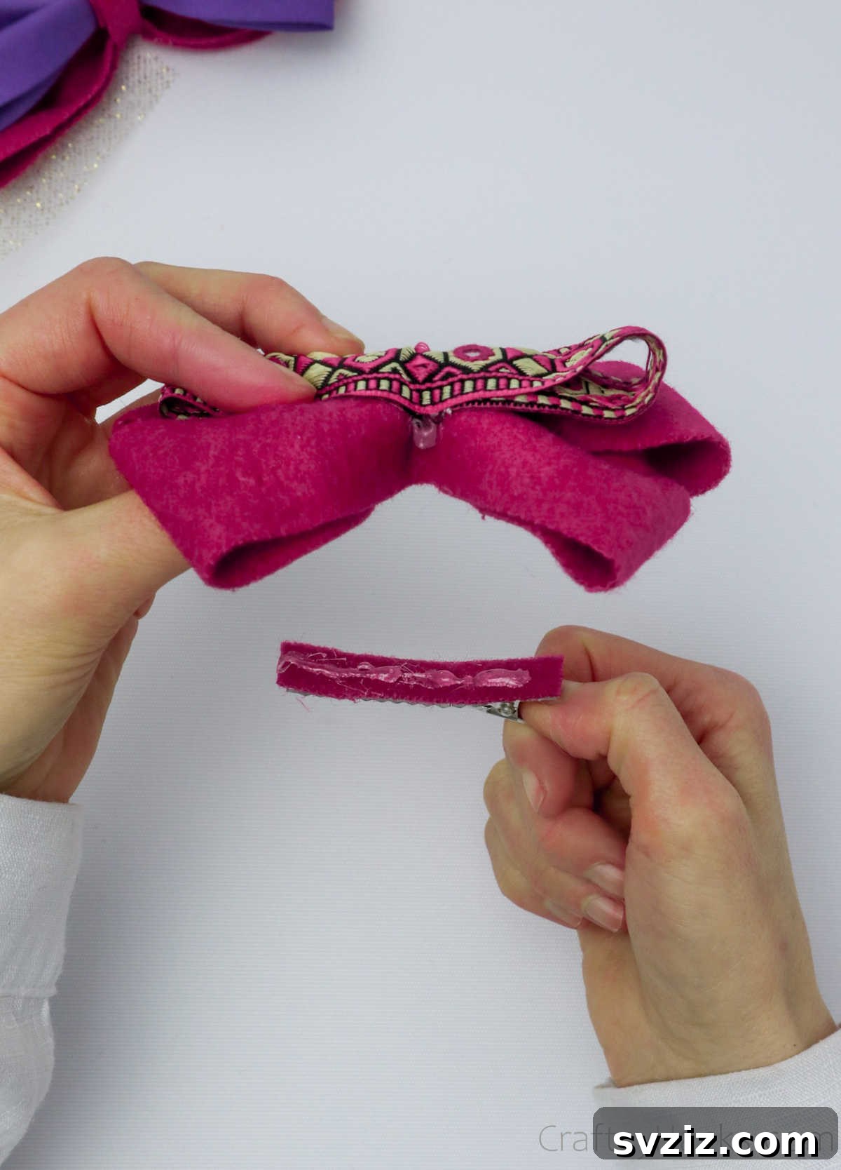 A crocodile clip being carefully attached to the back of a finished pink bow with hot glue, creating a wearable accessory