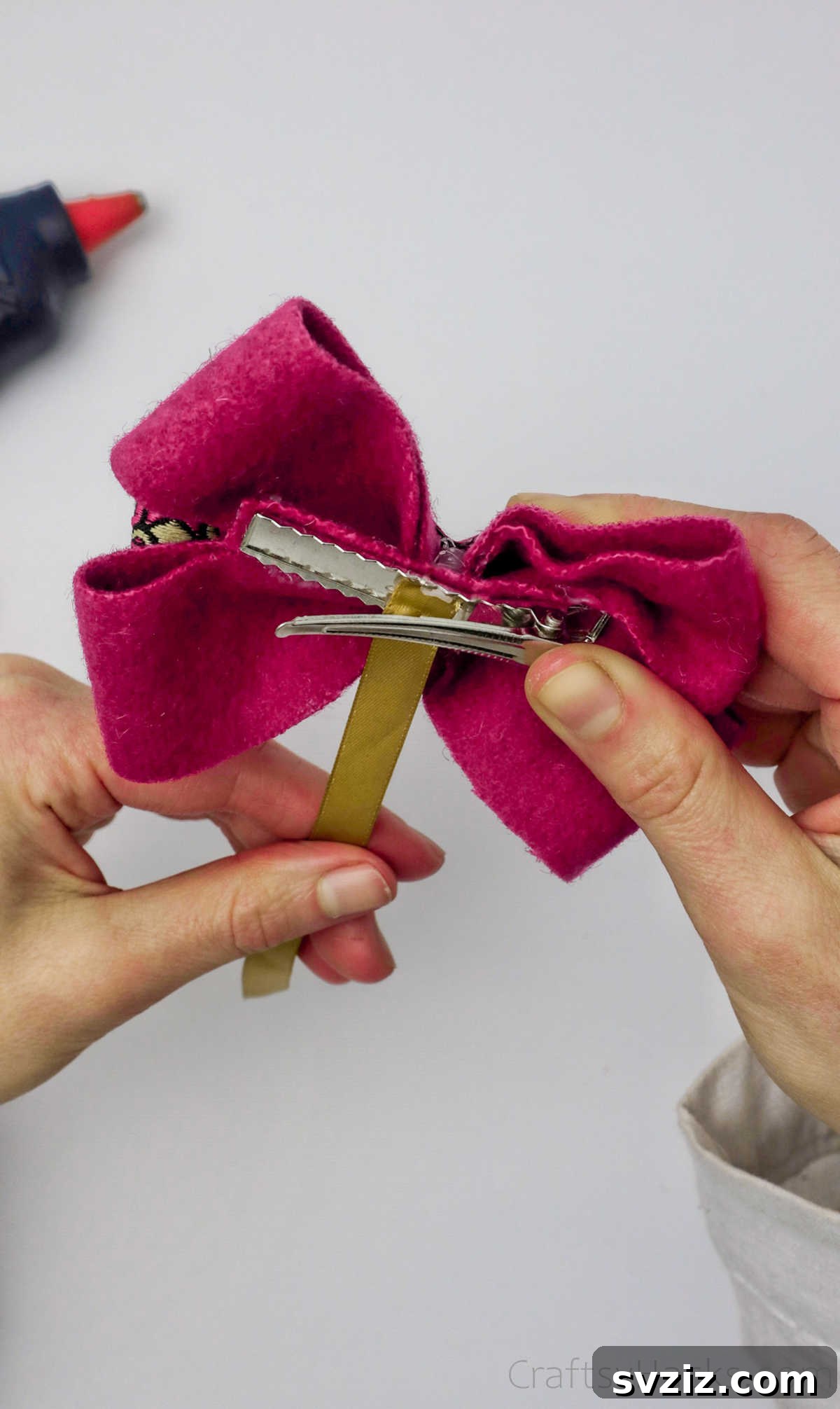 A yellow narrow ribbon being looped into the crocodile clip and wrapped around the center of the pink bow