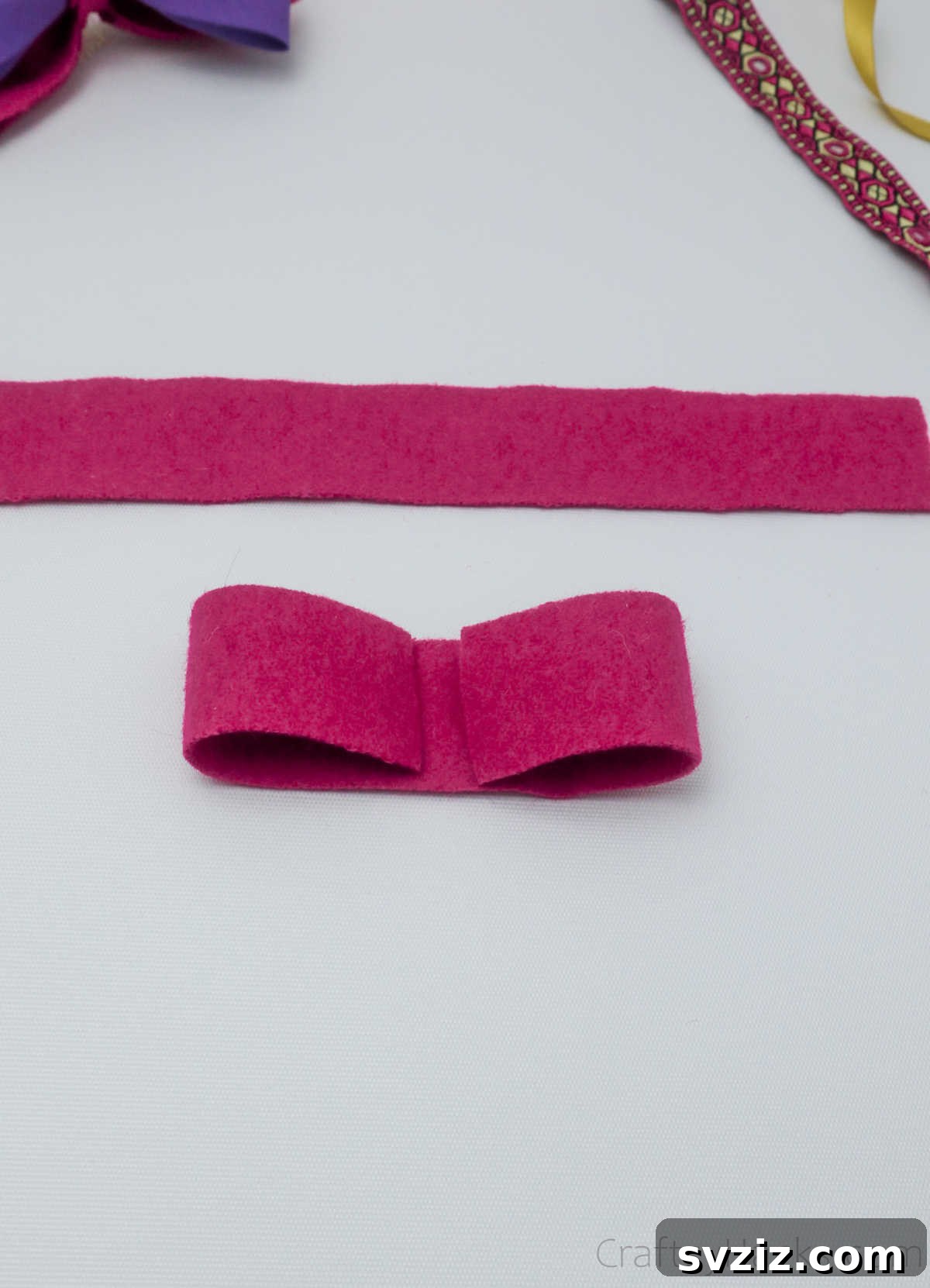 A pink felt strip meticulously folded to create the initial bow shape, ready for gluing