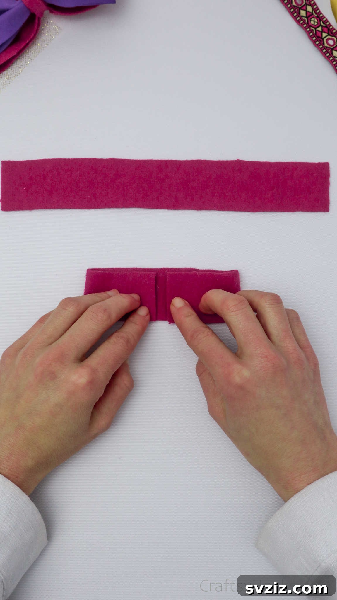The process of carefully gluing down the ends of a pink felt strip to form a neat bow component