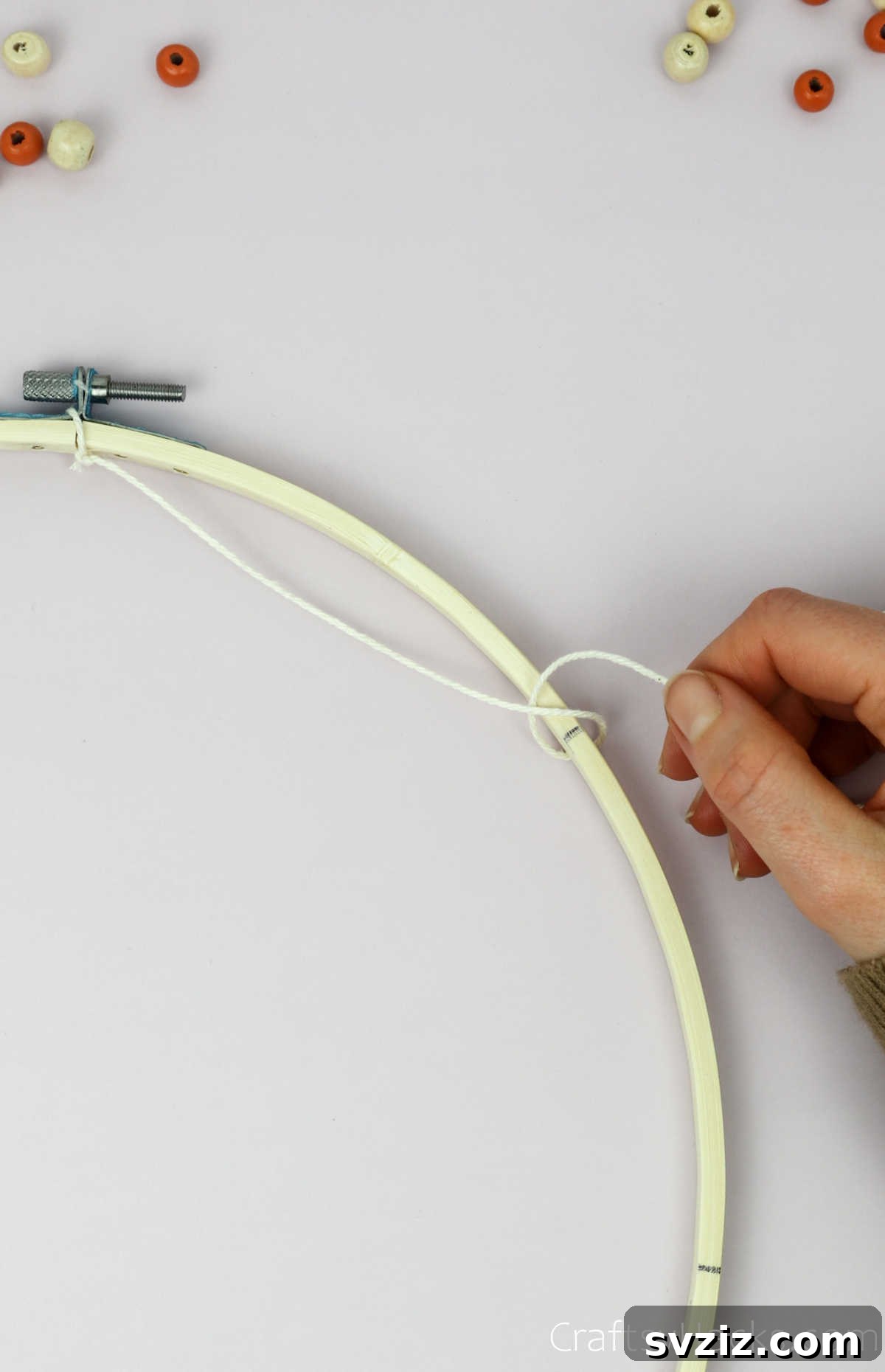 From Clutter to Charm: DIY Jewelry Storage 12 Detail of a hand tightening the looped beige cotton string around the embroidery hoop, ensuring it's snug and creating a uniform tension for the dreamcatcher web.