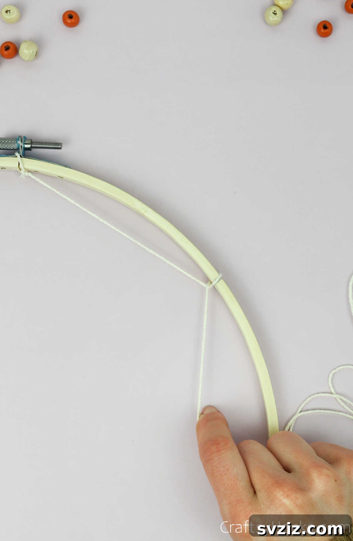 From Clutter to Charm: DIY Jewelry Storage 13 The first segment of the dreamcatcher web is established, with a taut beige cotton string extending from the initial knot and securely looped around the next marked point on the wooden hoop.