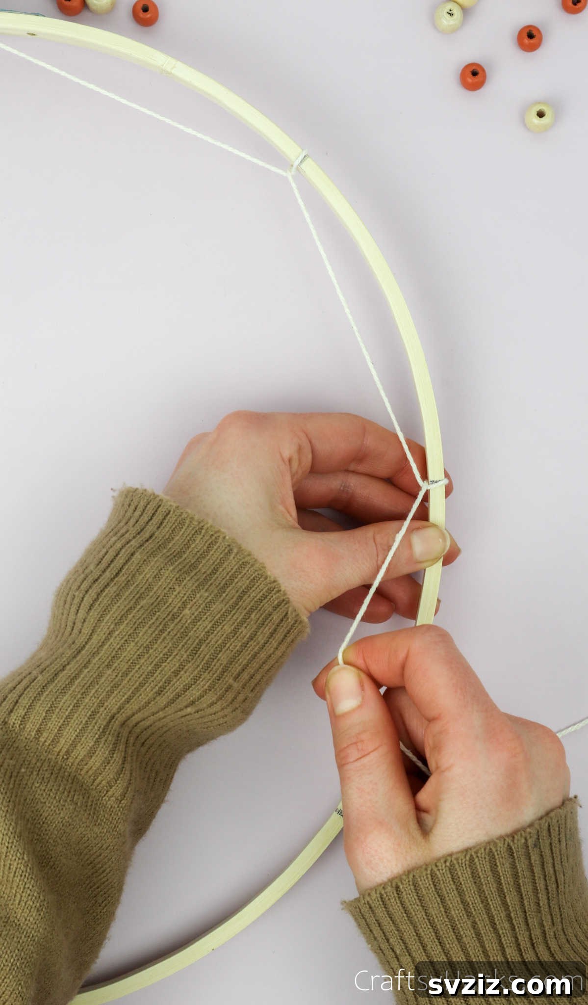 From Clutter to Charm: DIY Jewelry Storage 15 The first round of weaving is nearing completion, showing several segments of taut beige cotton string looped evenly around the embroidery hoop, forming the outer perimeter of the dreamcatcher web.