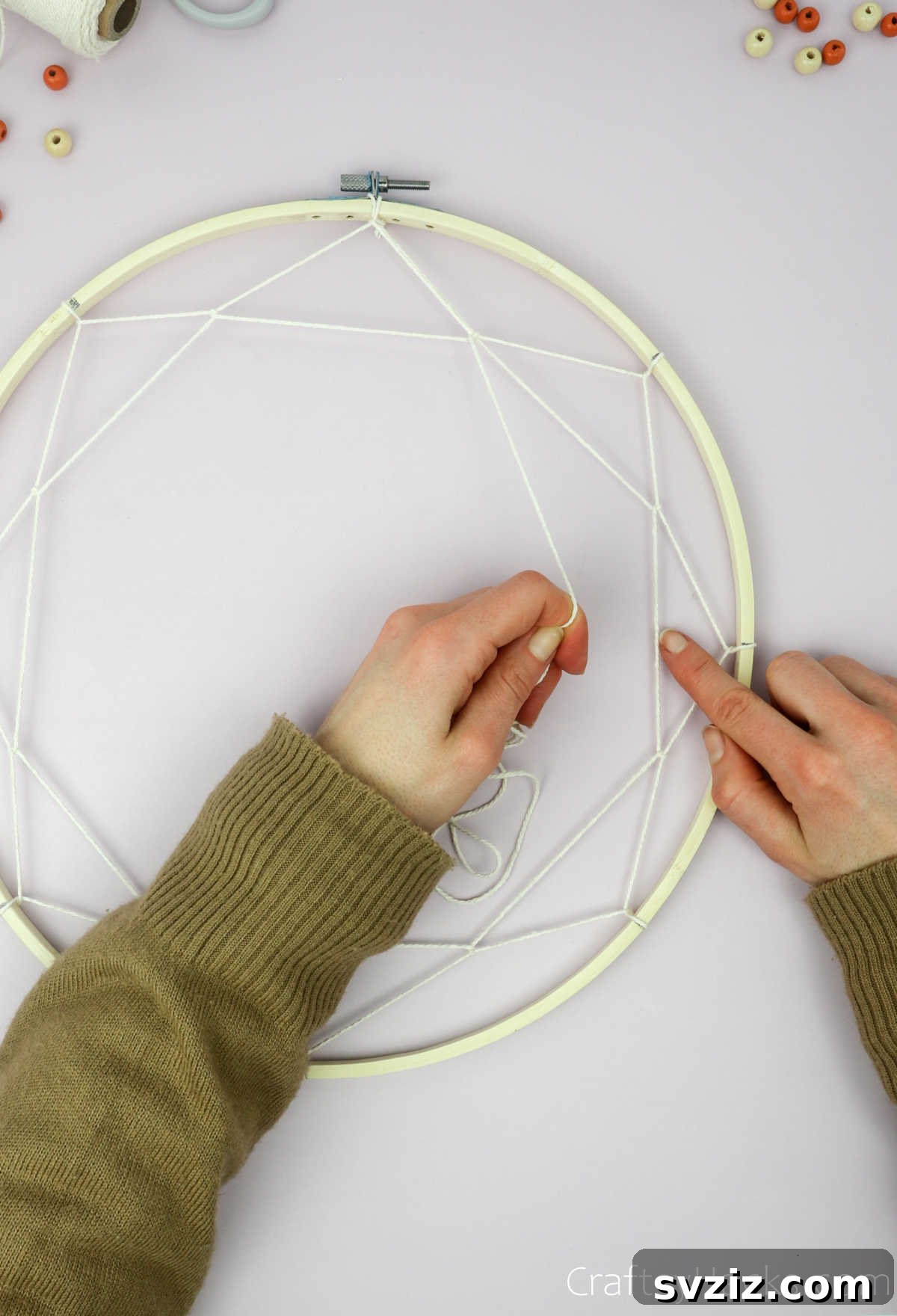 From Clutter to Charm: DIY Jewelry Storage 21 The third layer of string is being added to the dreamcatcher web, with the beige cotton string carefully looped through the previous row, forming a tightening spiral.