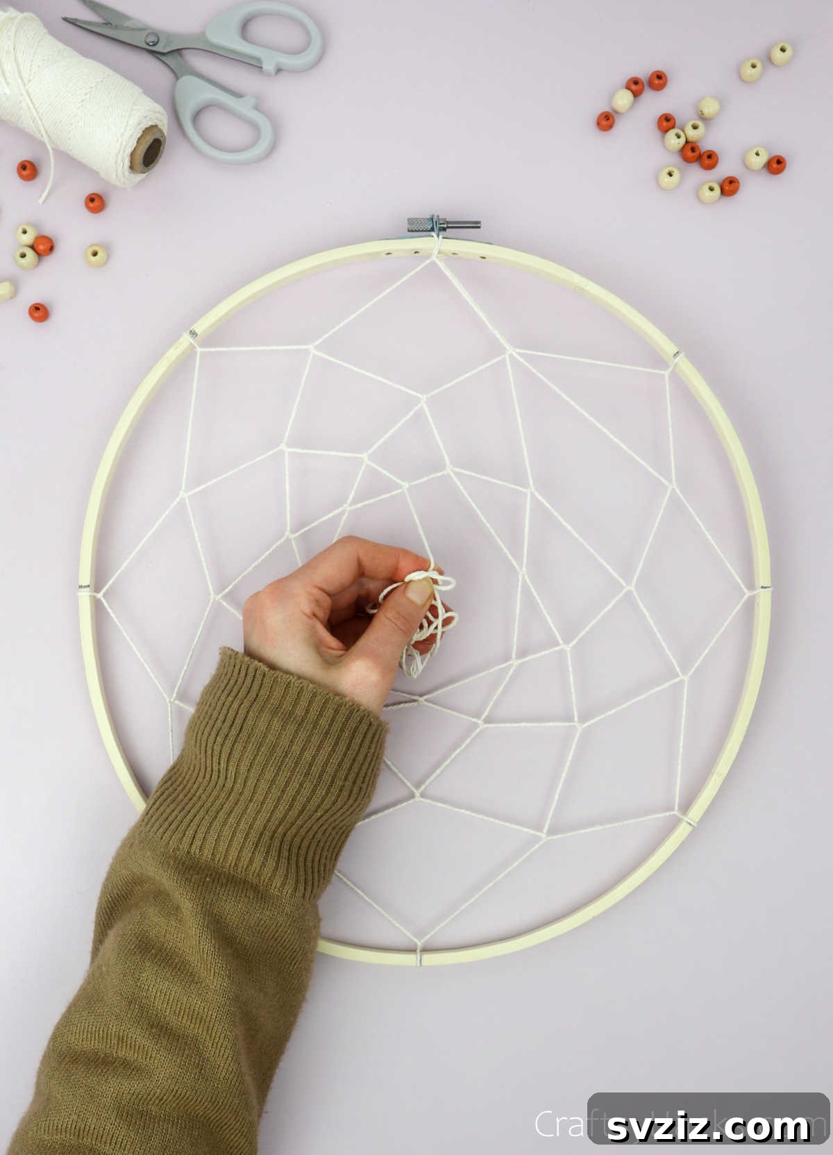 From Clutter to Charm: DIY Jewelry Storage 23 Several more layers of beige cotton string have been added to the dreamcatcher web, creating a tight, intricate pattern that spirals inwards towards the center of the hoop.