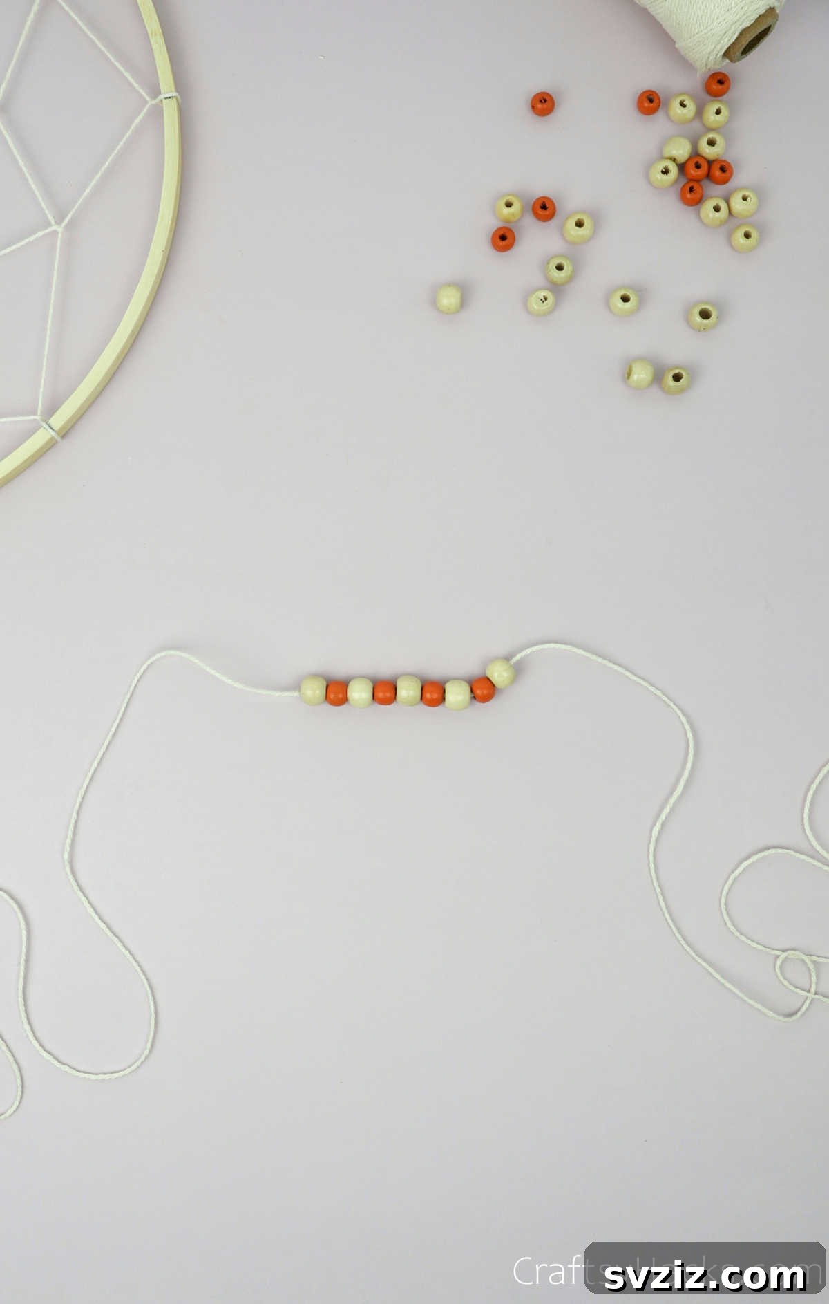 From Clutter to Charm: DIY Jewelry Storage 28 A beige cotton string adorned with a small, light-colored bead, tied to the bottom of the dreamcatcher's wooden hoop, demonstrating how to add decorative elements.