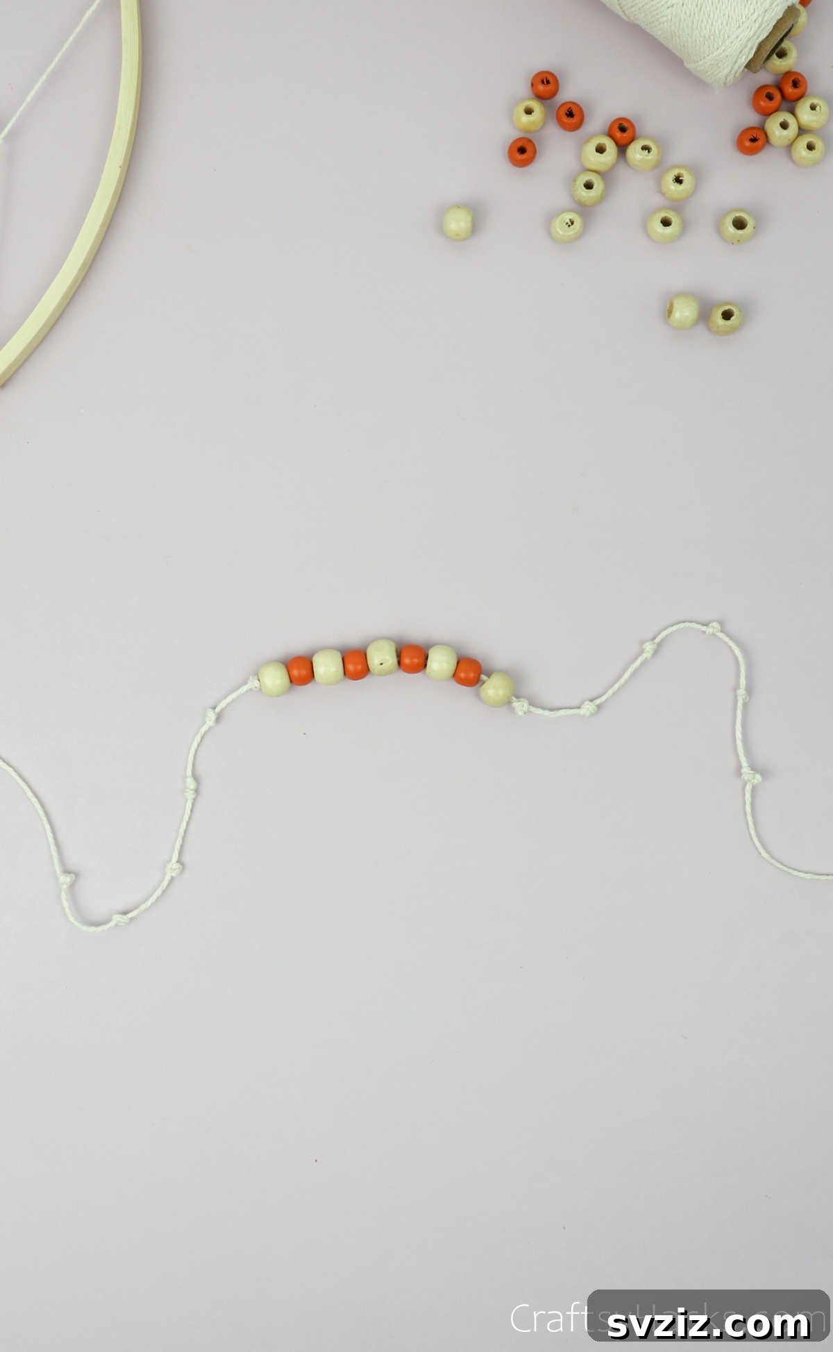 From Clutter to Charm: DIY Jewelry Storage 29 A close-up of a small, decorative bead secured by multiple knots on a beige string, which is then tied to the wooden hoop of the DIY jewelry organizer.