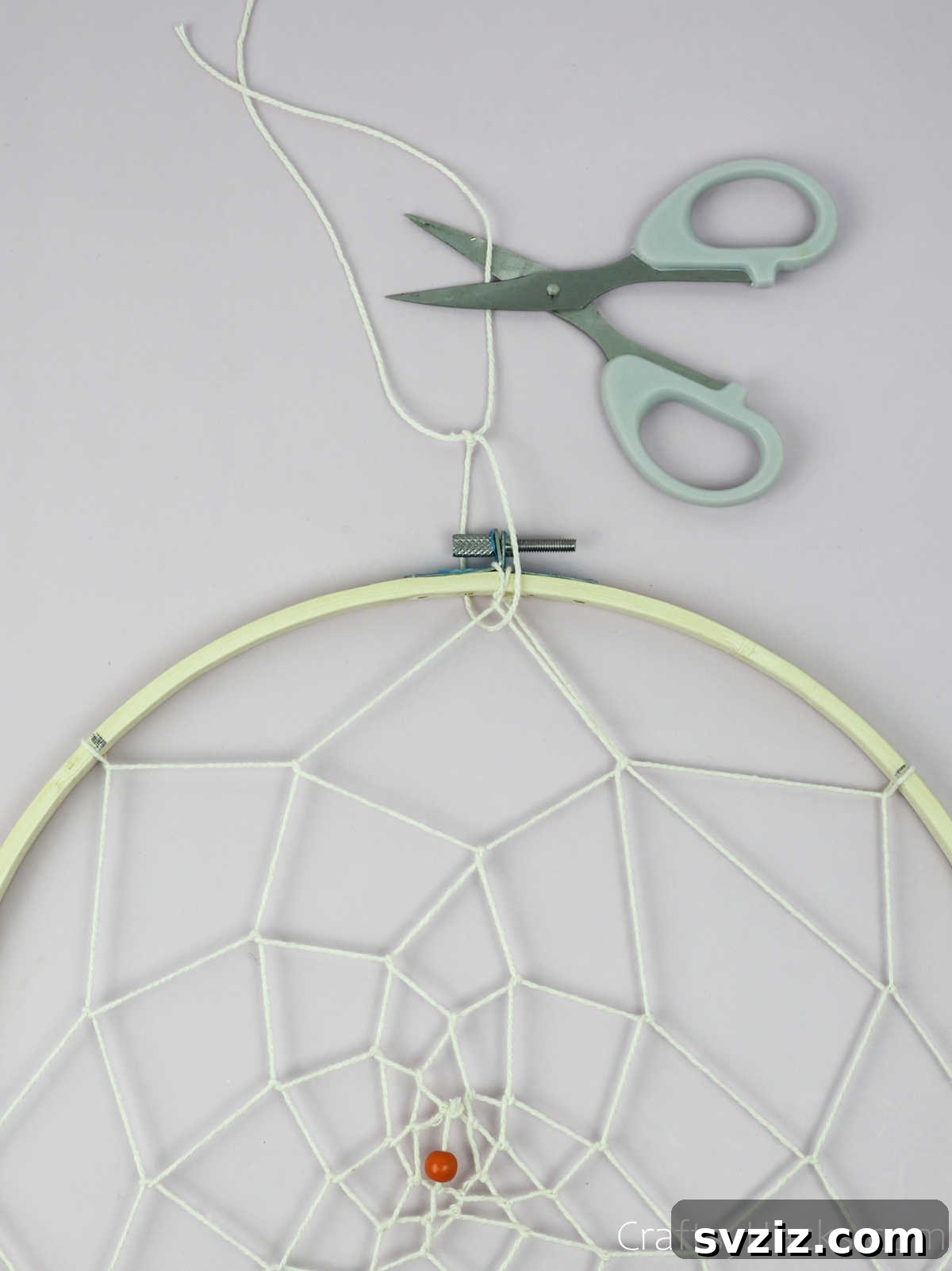 From Clutter to Charm: DIY Jewelry Storage 32 A hand cutting a length of beige cotton string, preparing to create the hanging loop for the DIY jewelry organizer at the top of the hoop.