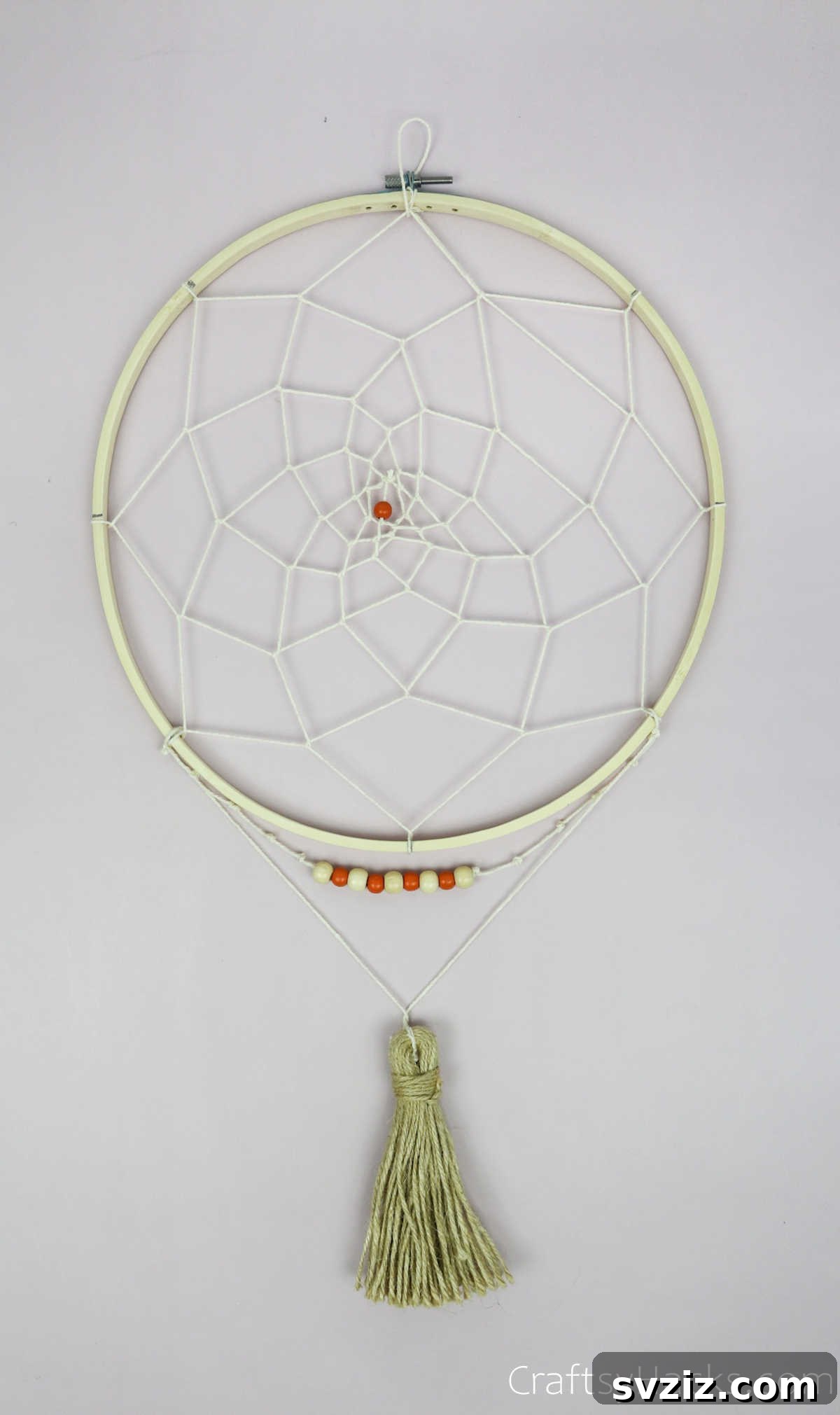 From Clutter to Charm: DIY Jewelry Storage 33 A beautifully completed DIY dreamcatcher jewelry organizer, featuring a white woven web within a wooden hoop, accented with beads and tassels, ready to be adorned with jewelry.
