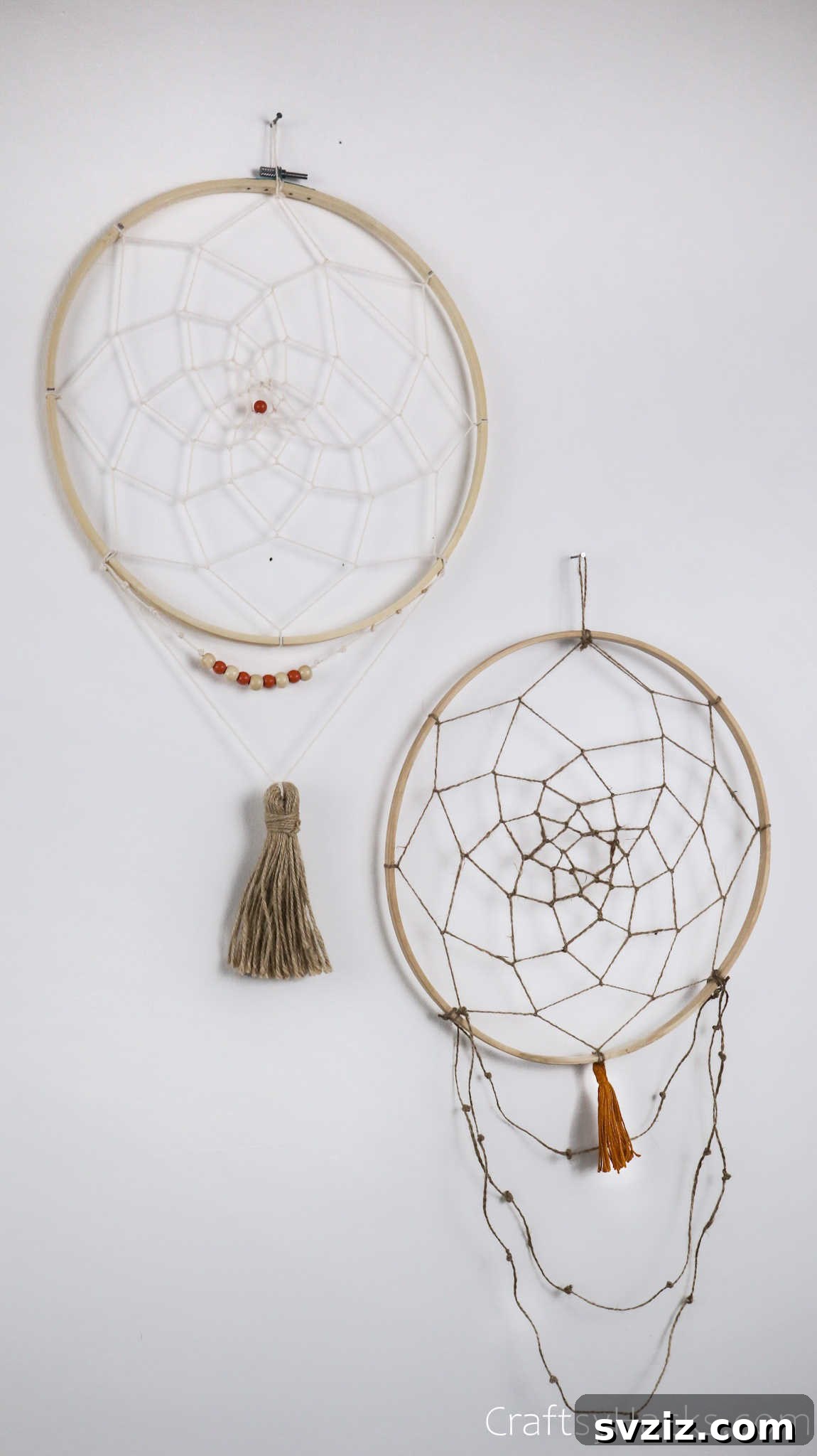 From Clutter to Charm: DIY Jewelry Storage 35 Two completed DIY dreamcatcher jewelry organizers hanging against a pale wall, ready for use. One features a simple white web, the other a more detailed beige and white pattern, both framed by wooden hoops.