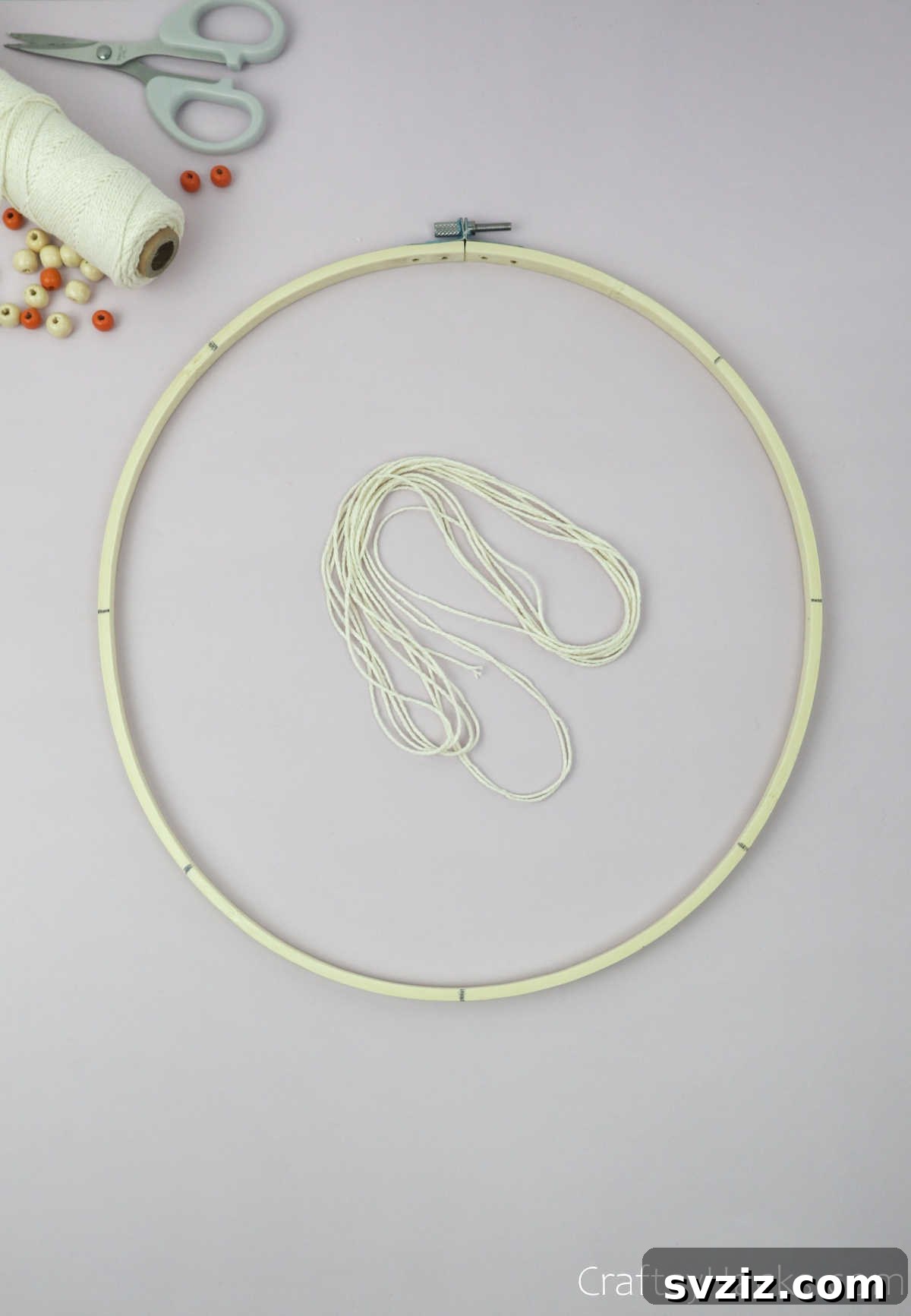 From Clutter to Charm: DIY Jewelry Storage 8 A hand holding a bundle of beige cotton string, positioned over an embroidery hoop, ready to begin the weaving process.