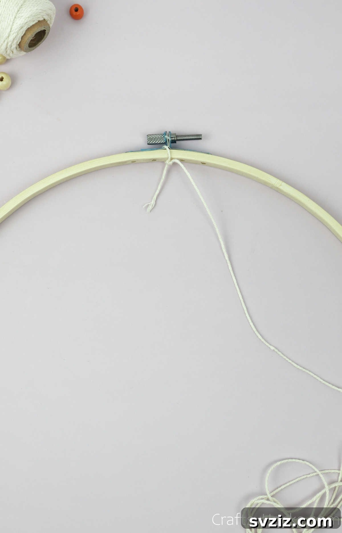 From Clutter to Charm: DIY Jewelry Storage 9 A close-up of a hand tying a secure knot with beige cotton string around the top (12 o'clock position) of a wooden embroidery hoop, marking the starting point of the dreamcatcher web.