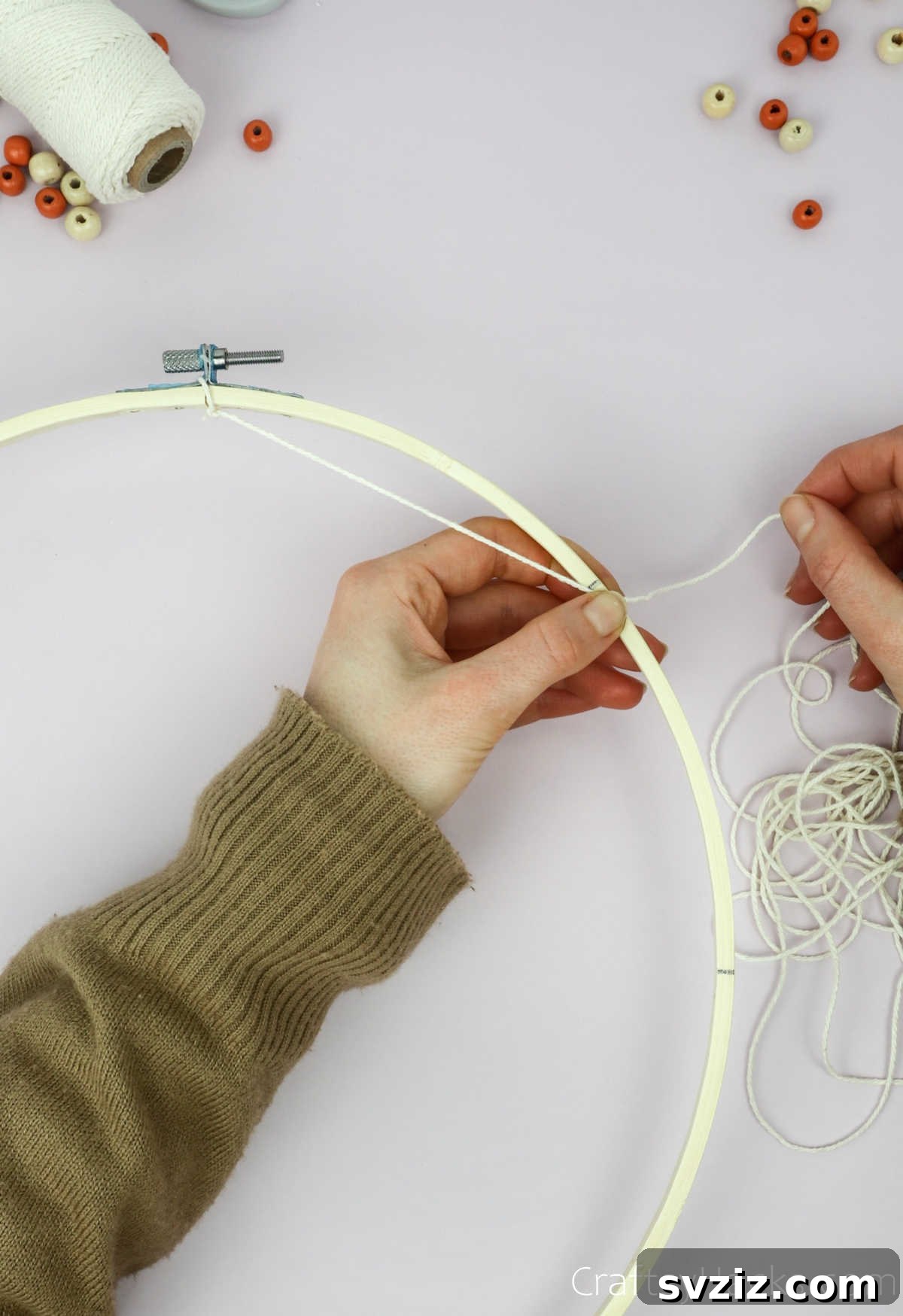 From Clutter to Charm: DIY Jewelry Storage 10 A hand demonstrates looping a beige cotton string over and around the wooden embroidery hoop, creating the first attachment point for the dreamcatcher web.