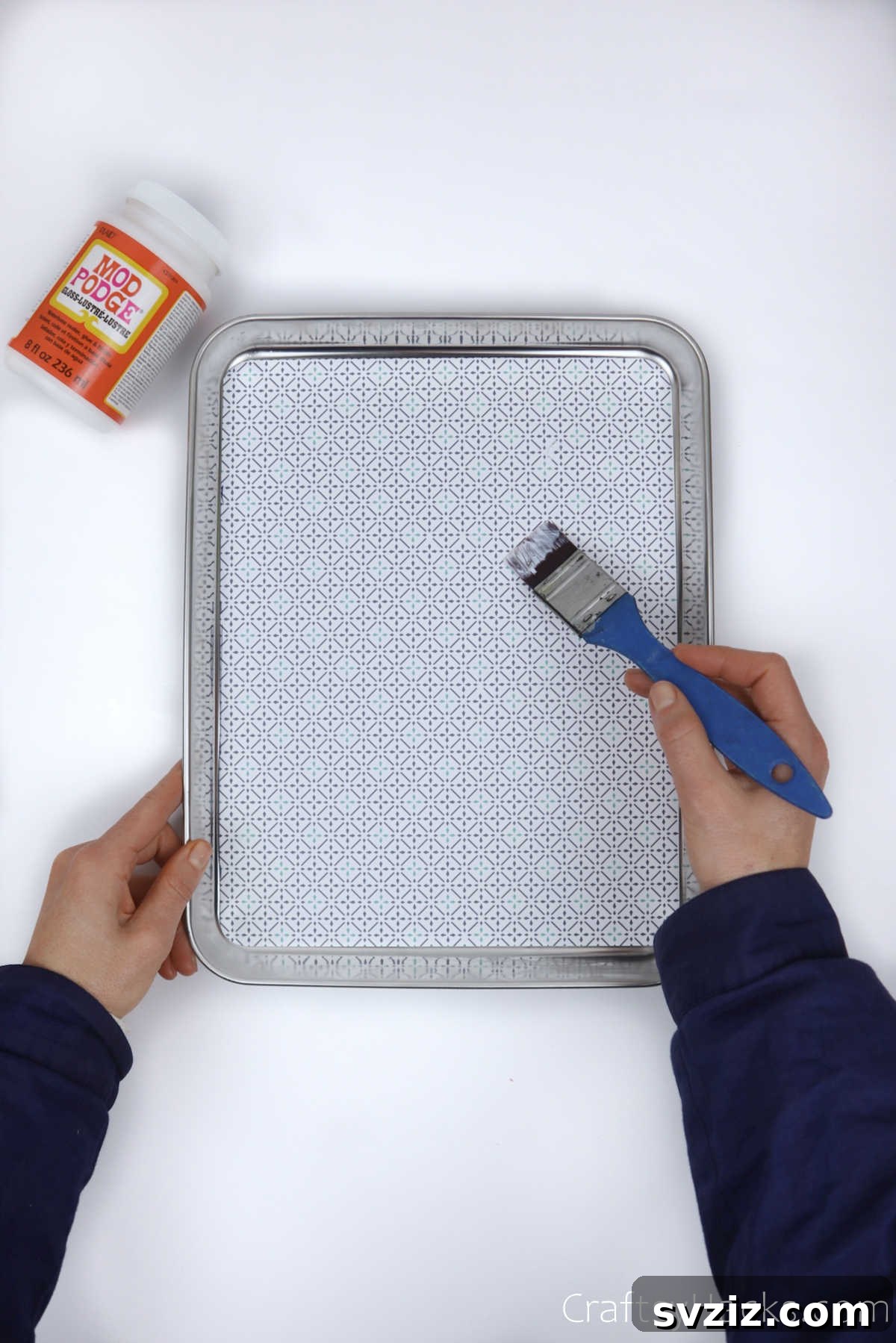Spreading Mod Podge over decorative paper on a tray