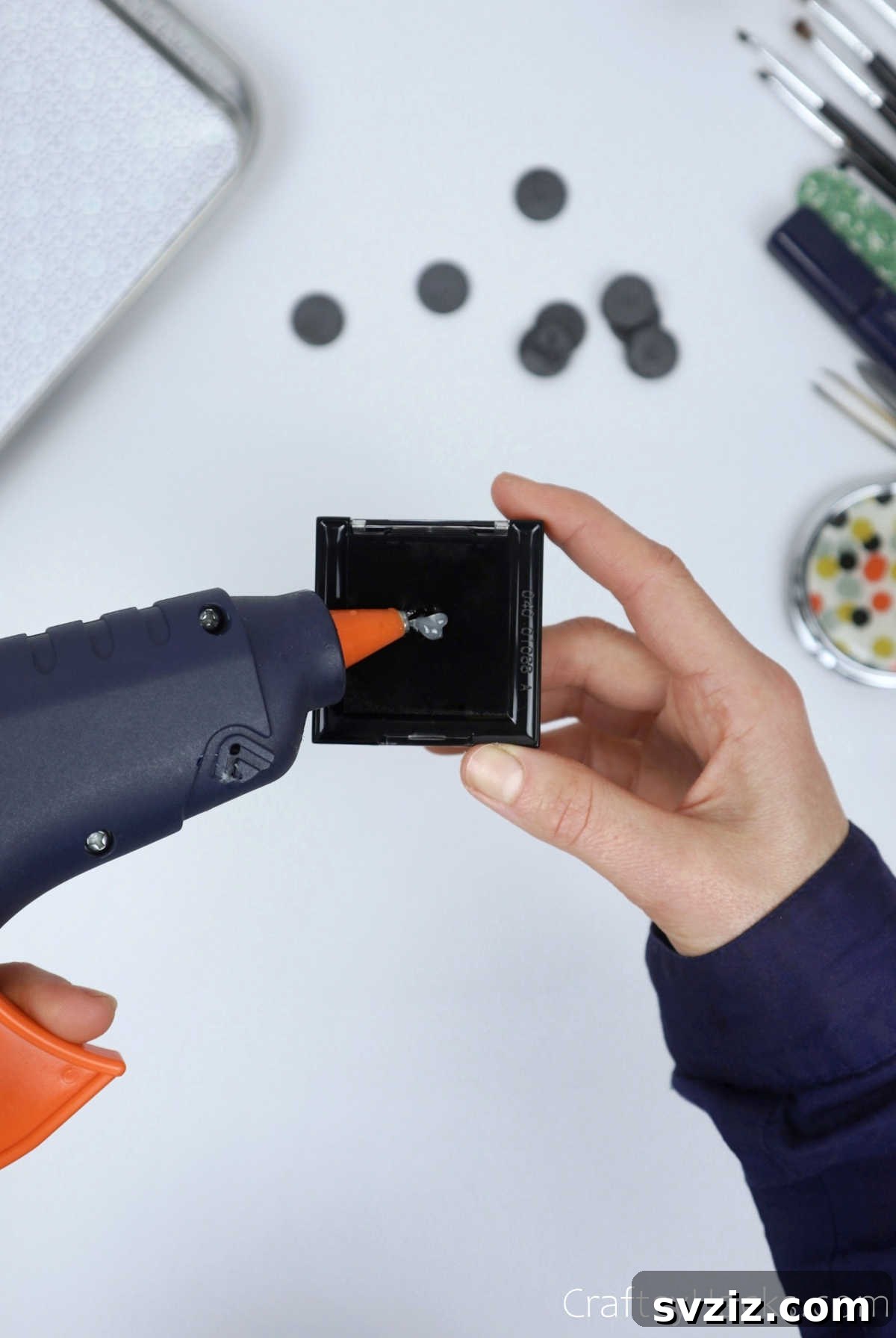 Applying hot glue to the back of a makeup compact