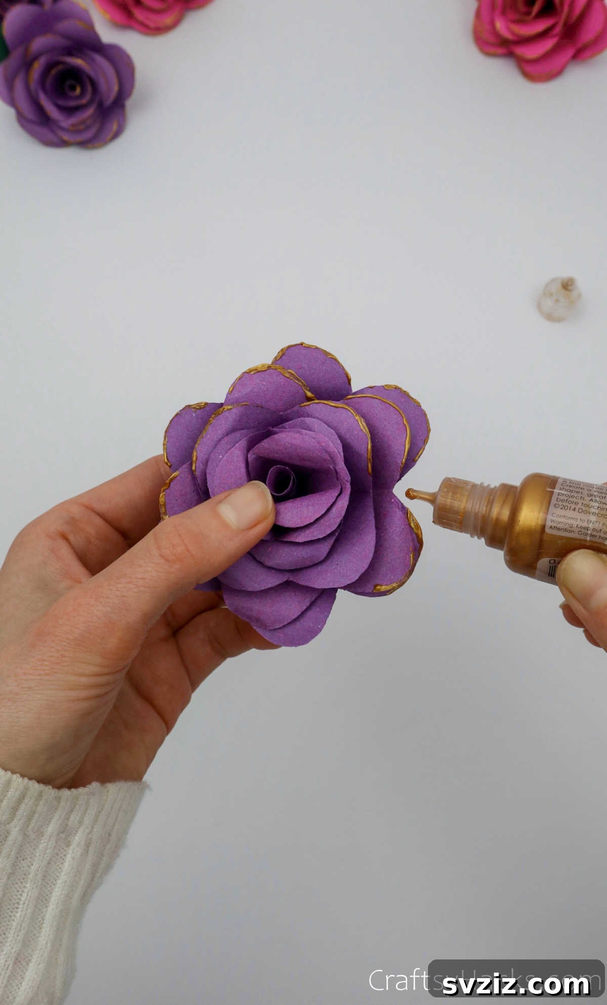 Crafting Beautiful Paper Blooms 29 A hand adding gold glitter glue to the edges of a purple paper flower for a decorative finish