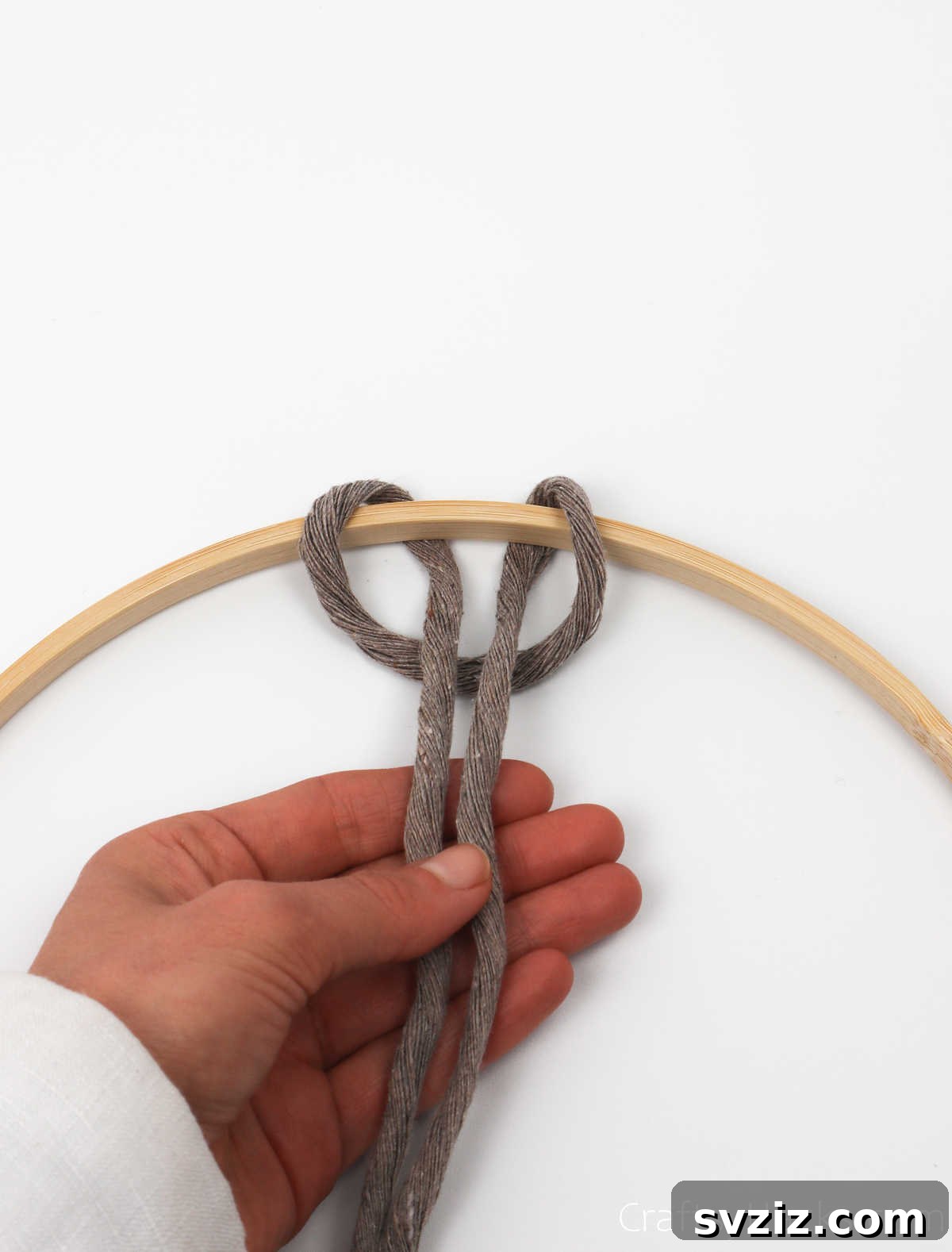 Pulling the two loose ends of the cord through the loop to tighten the first knot on the hoop.