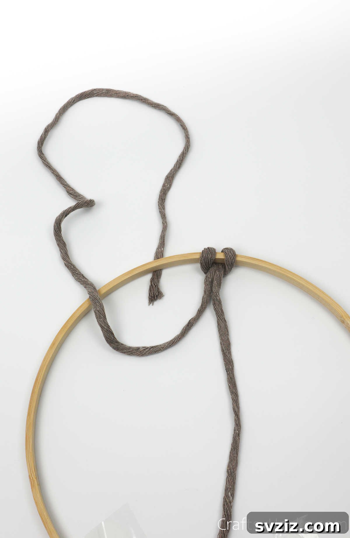 The left string of the cord being looped over and under the hoop to create a secondary knot.