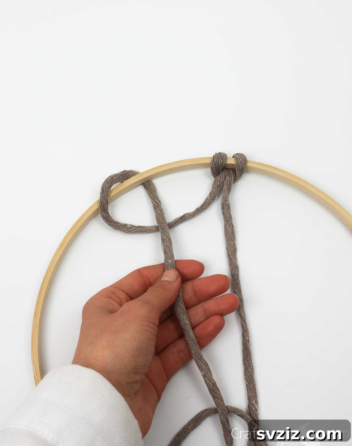 The end of the left string being pulled through the loop, completing the second knot on the dreamcatcher hoop.