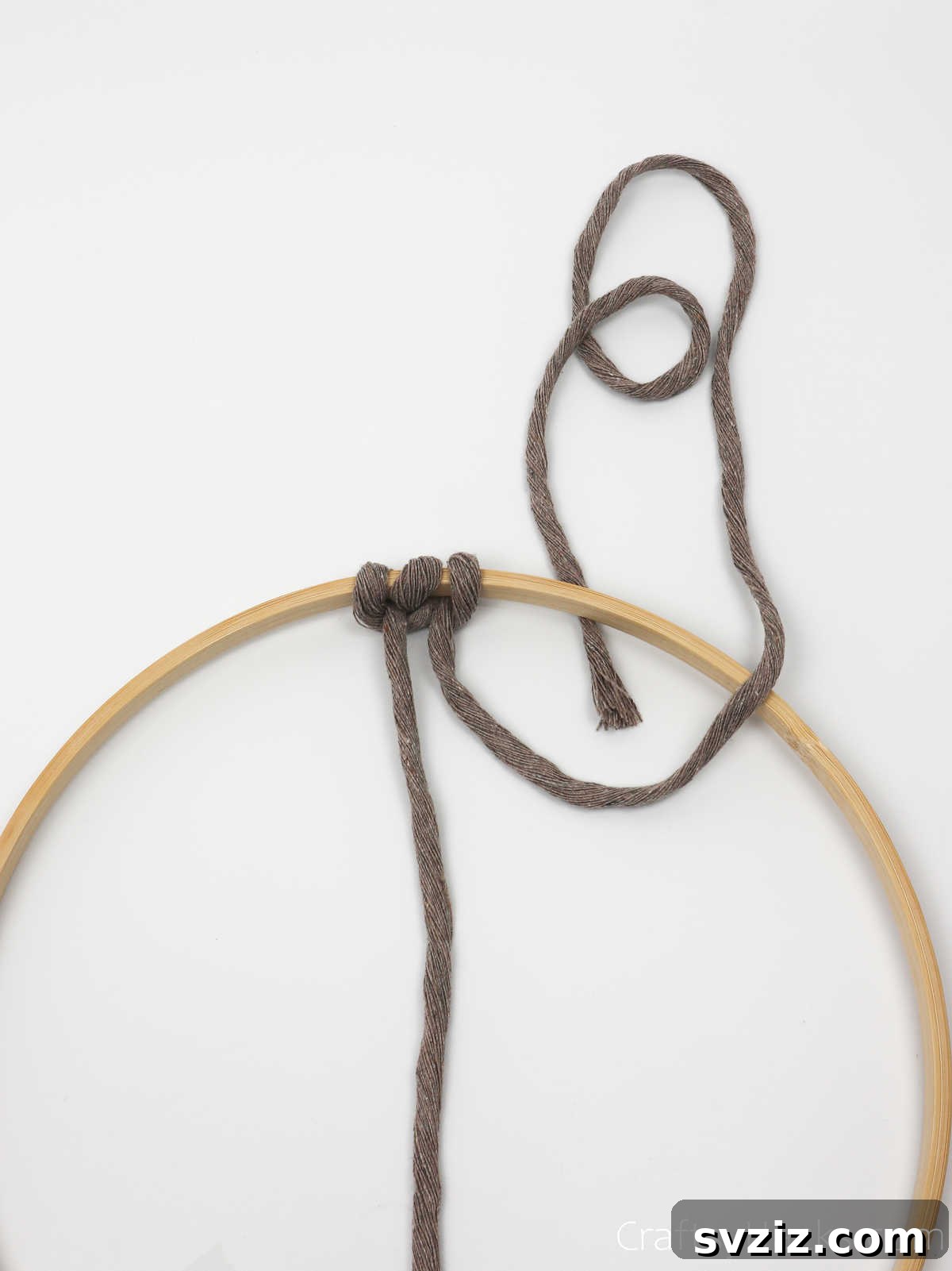 The right string of the cord being looped to complete the symmetrical two-part knot set on the hoop.