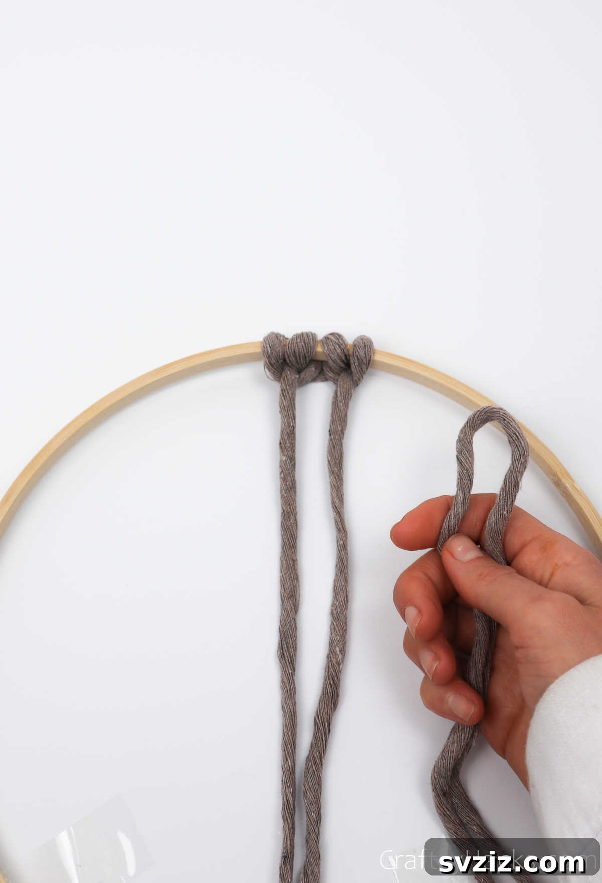 Adding another cappuccino-colored cord to the hoop, preparing for the next set of knots.