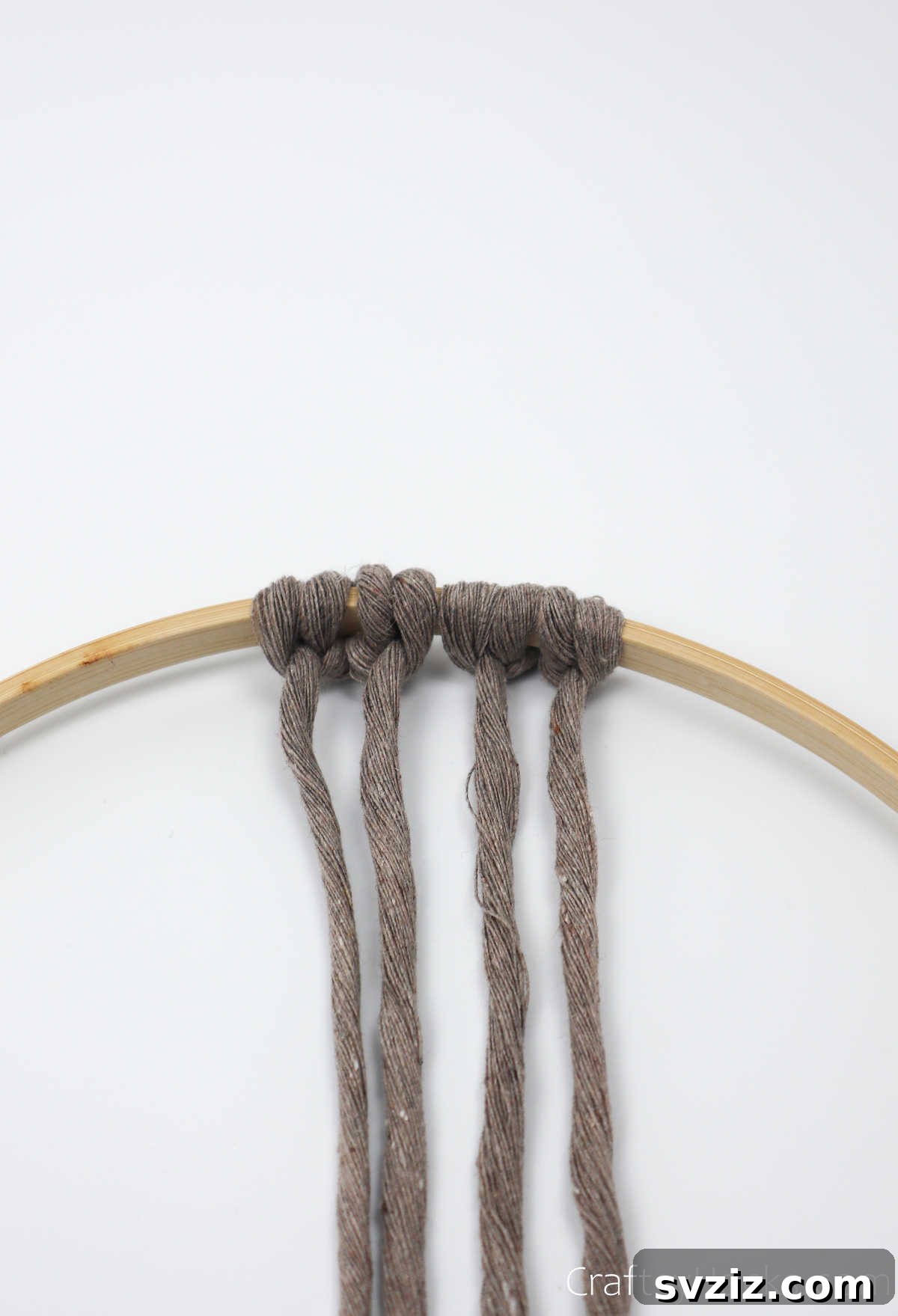 Two sets of cappuccino-colored knots now visible on the hoop, showing the growing pattern.