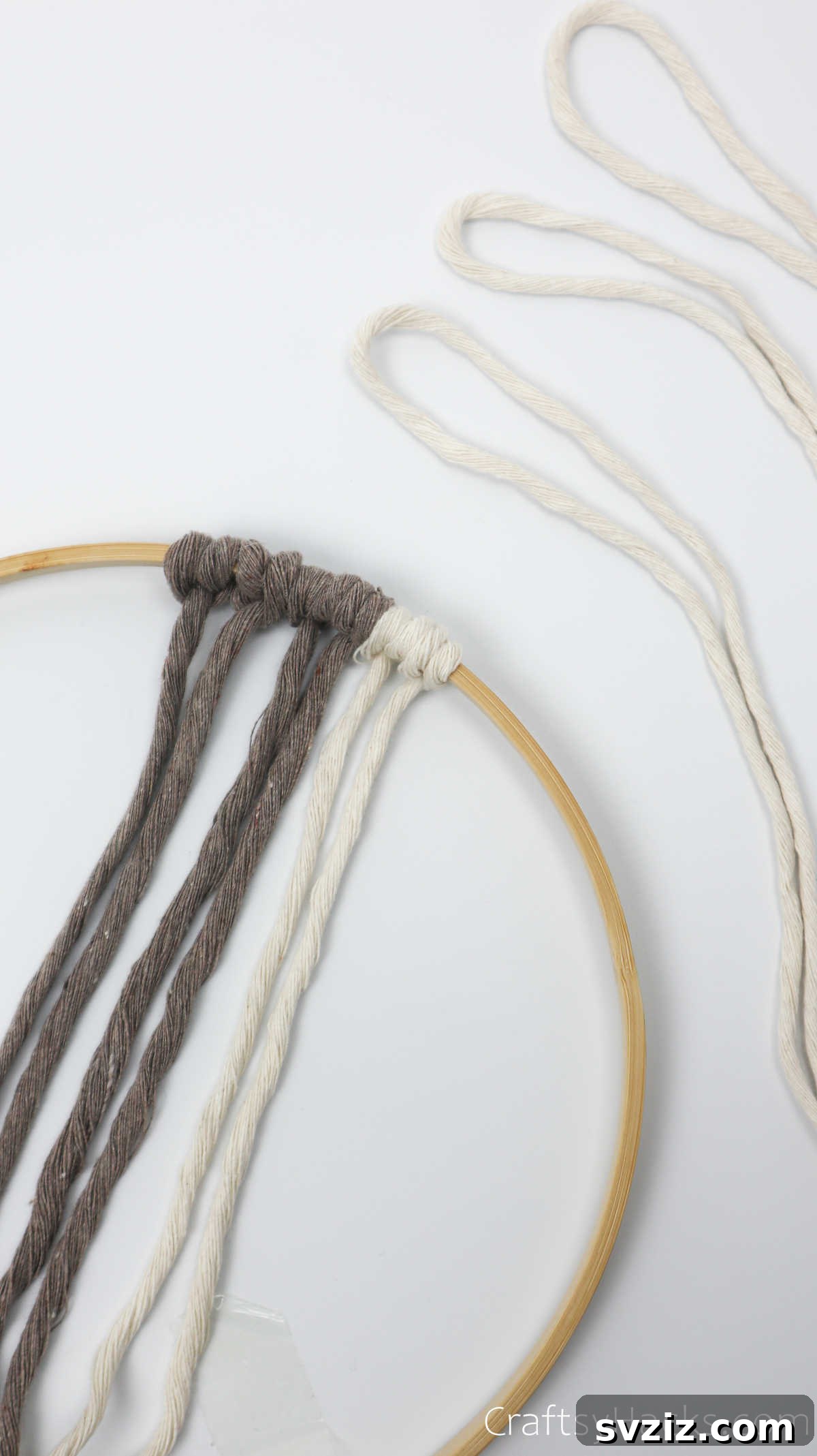 Adding the first cream-colored knot to the dreamcatcher hoop, starting a new color segment.