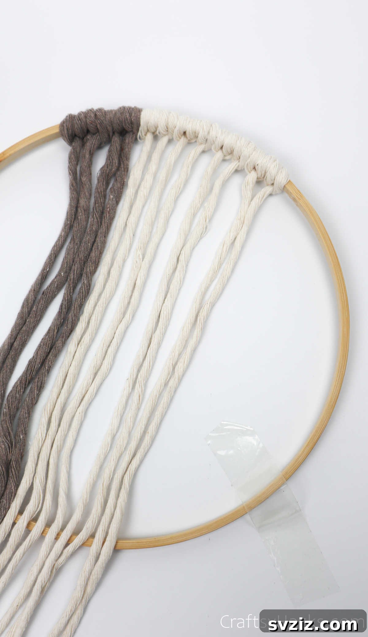 Four cream-colored cords now knotted onto the hoop, showcasing the evolving color pattern.