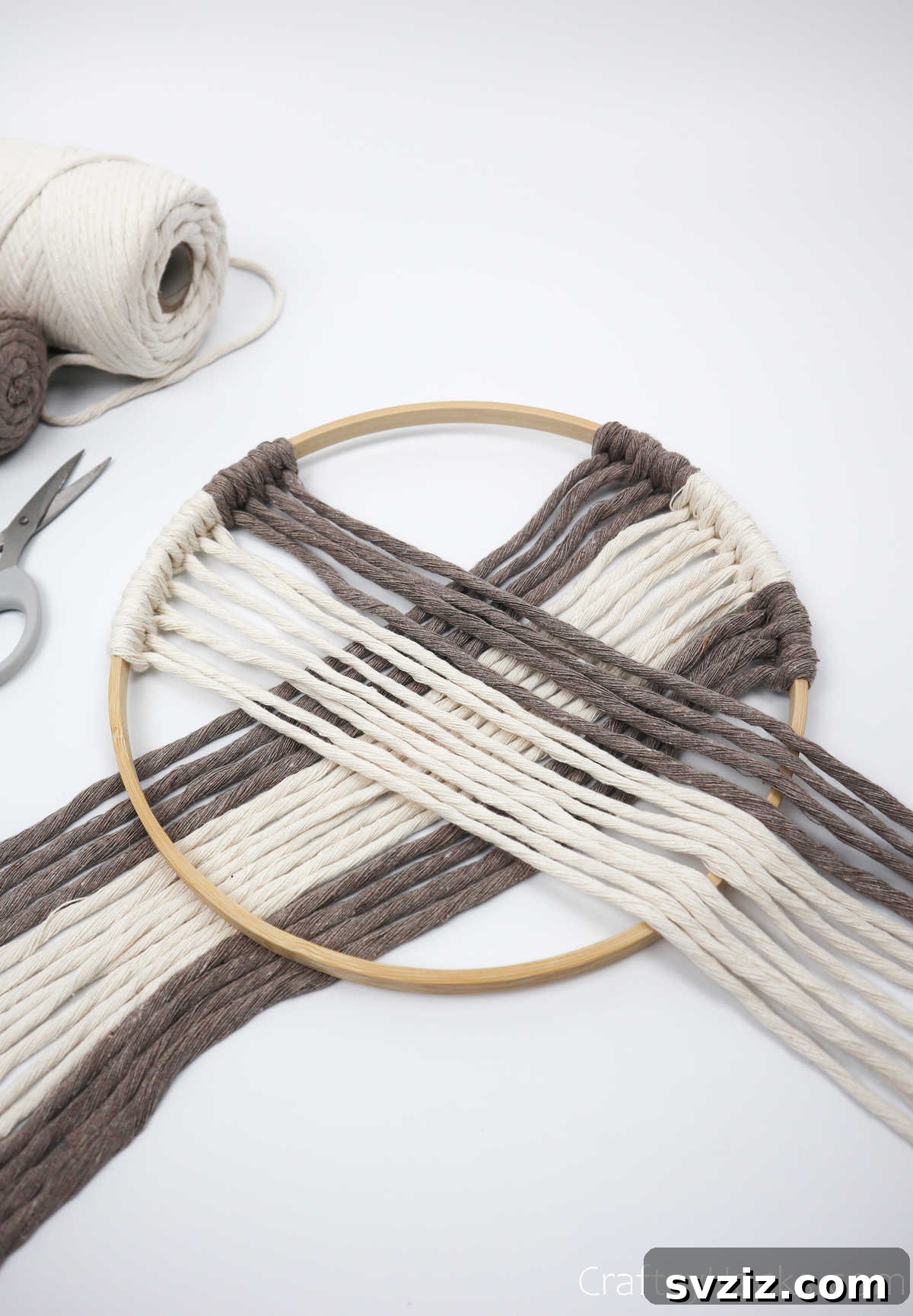 The symmetrical pattern of cords now spans across the top of the hoop, with cords hanging from both sides.