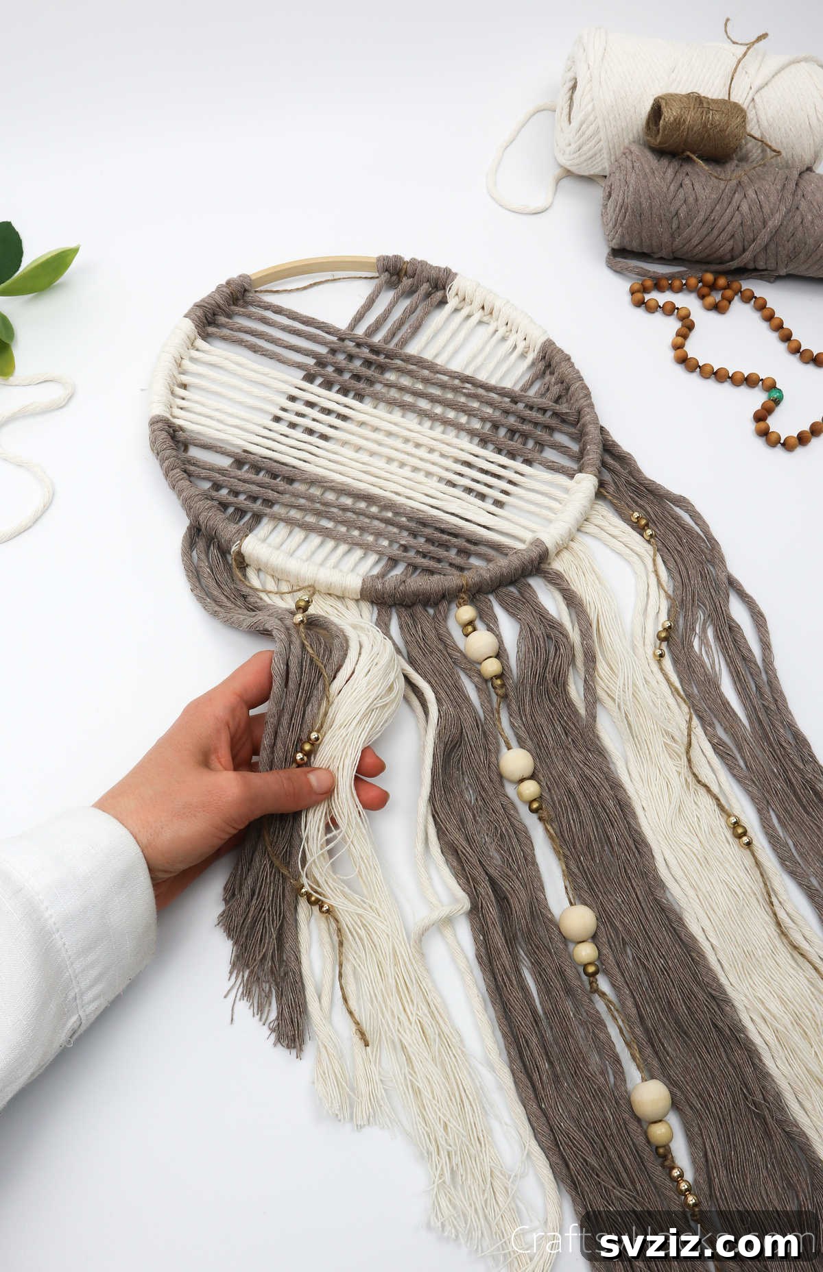 A person holding the finished dreamcatcher, showcasing the neatly combed and trimmed ends.